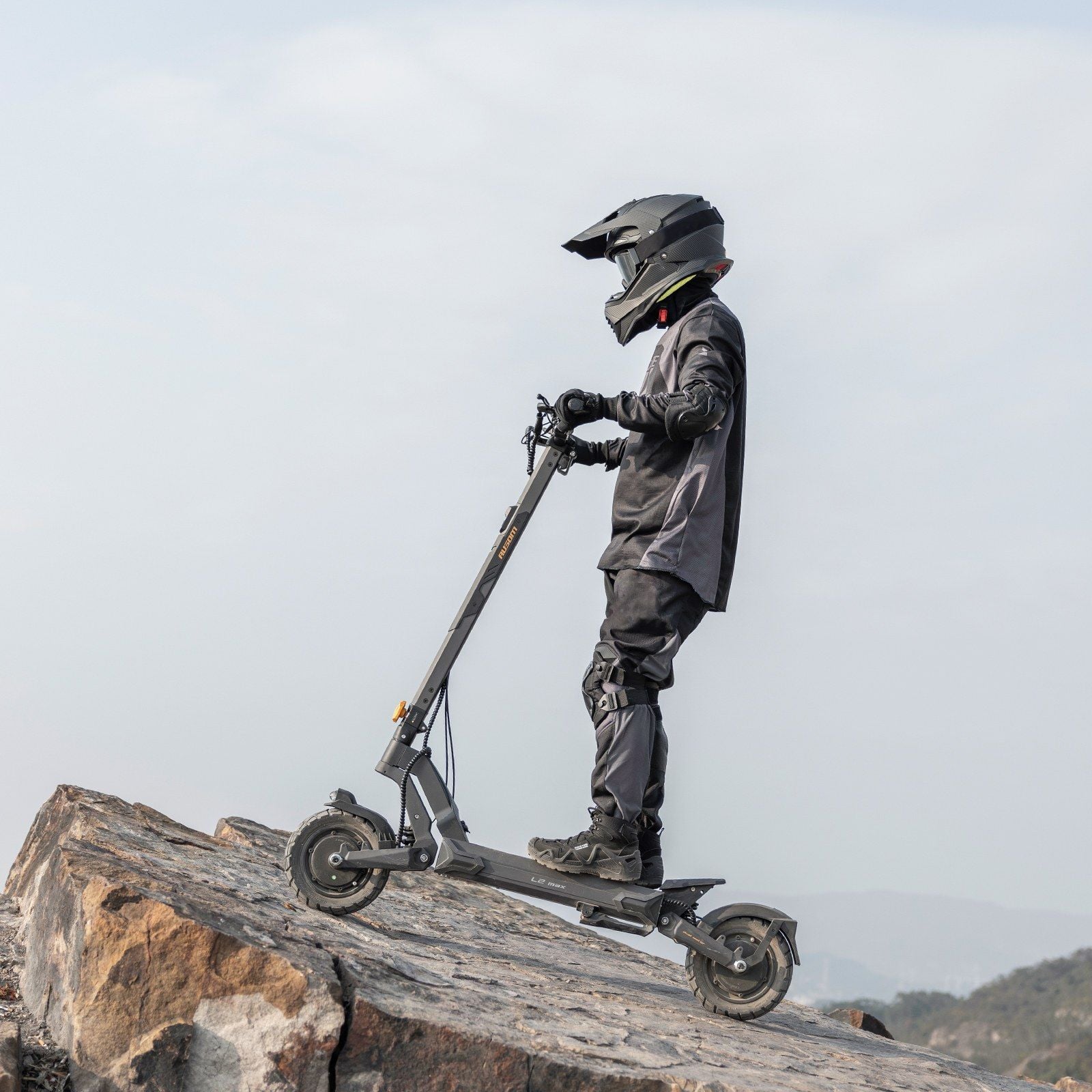 Rider in a full-face helmet on an Ausom L2 Max Dual Motor electric scooter on rocky ground