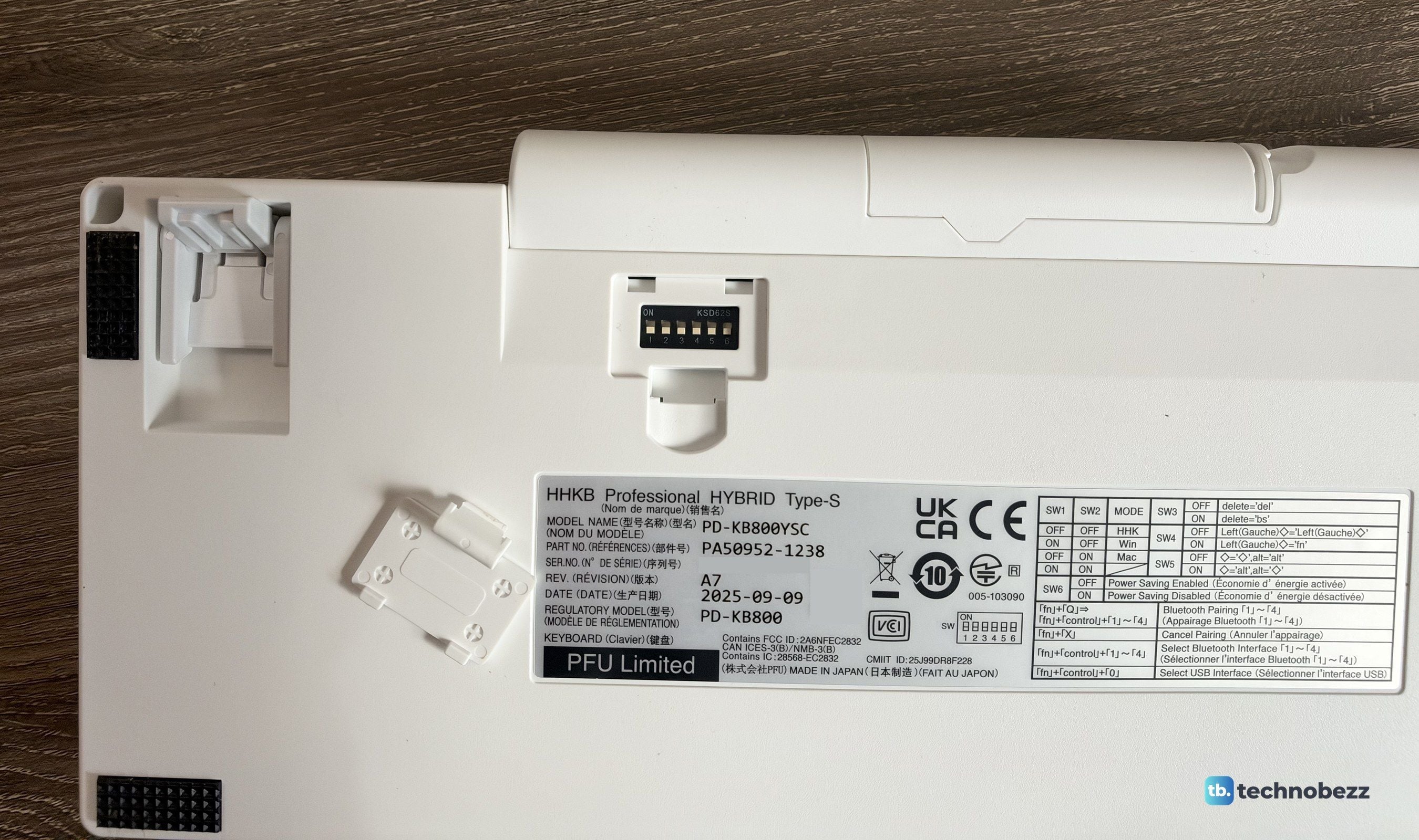 Underside of the HHKB with the DIP switch cover removed, a flip-out foot, and the product label