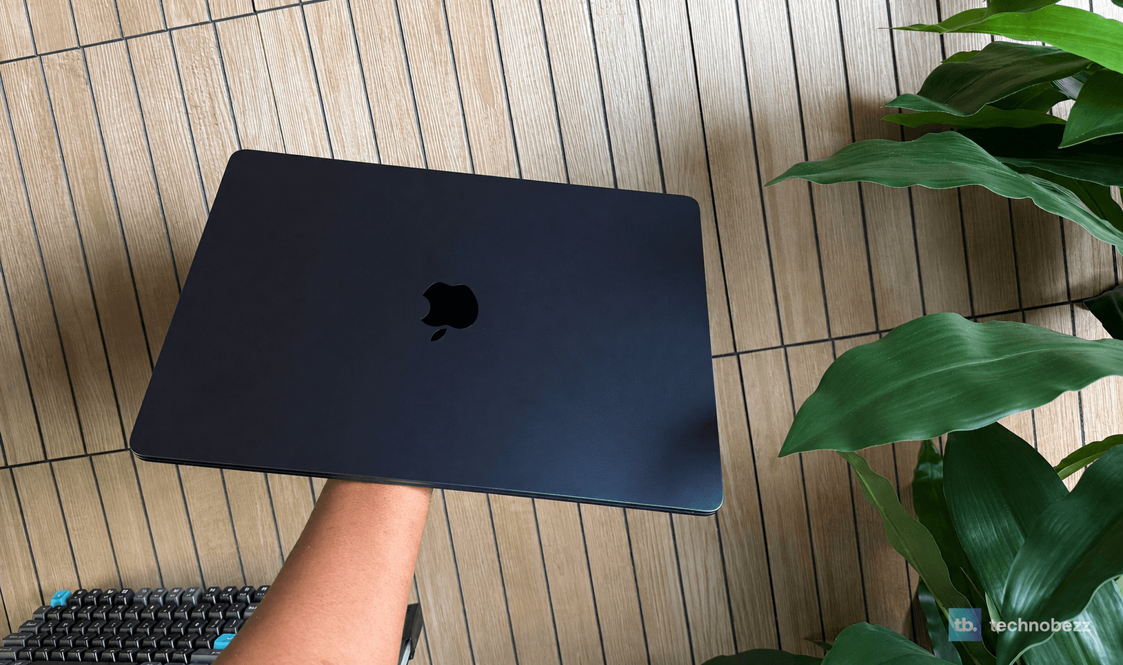 15-inch MacBook Air M5 in Midnight held closed beside a green plant