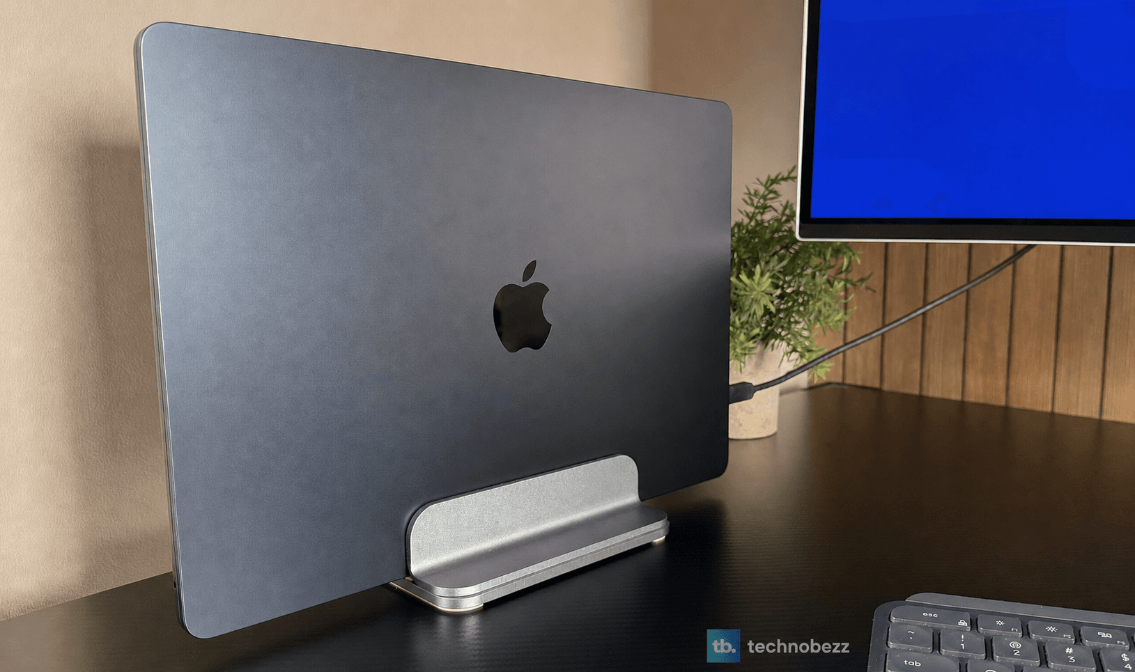 Rear view of the Midnight MacBook Air M5 on a vertical stand beside a monitor