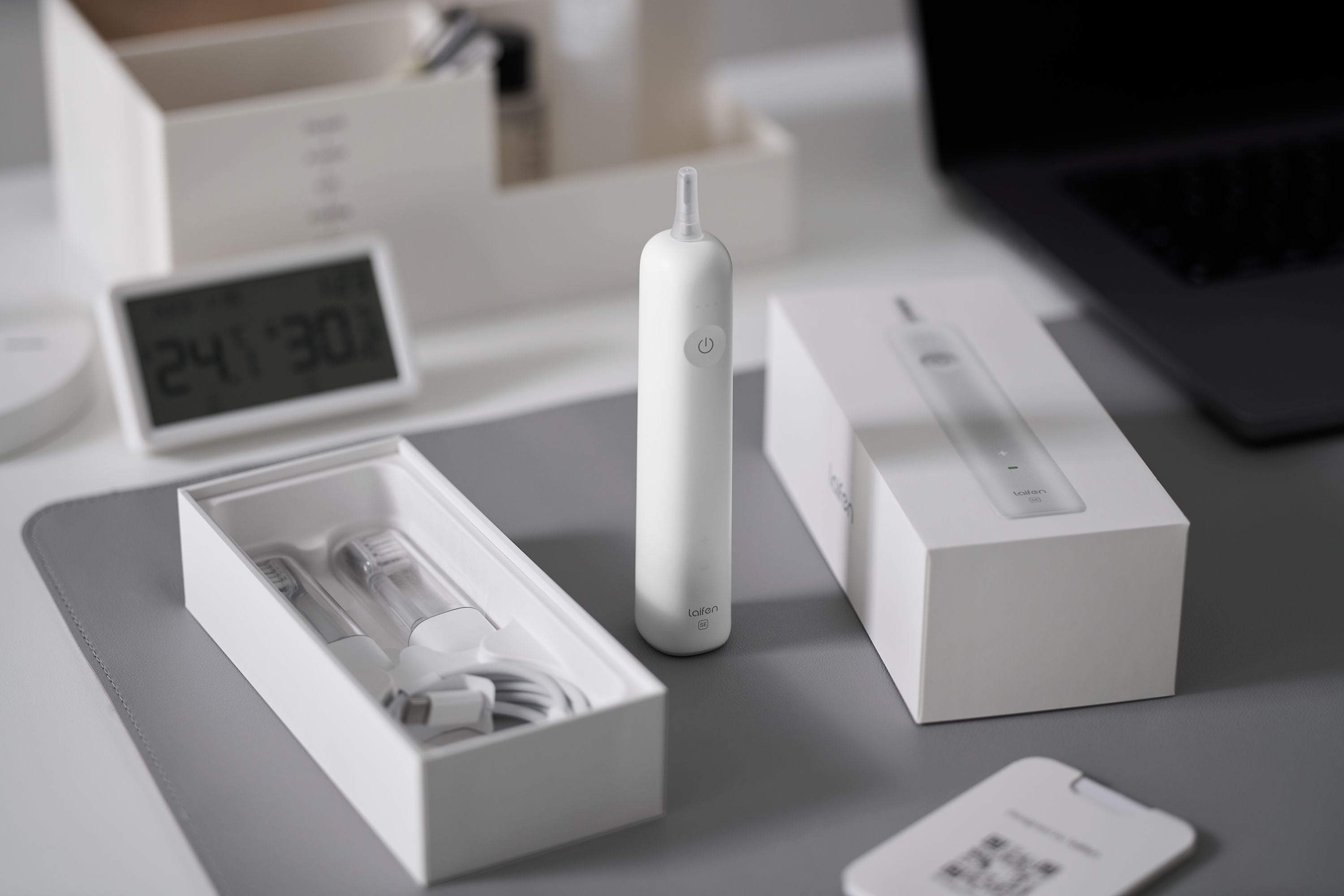 The white Laifen Wave Special electric toothbrush standing beside its box, spare brush heads, and charging cable on a desk