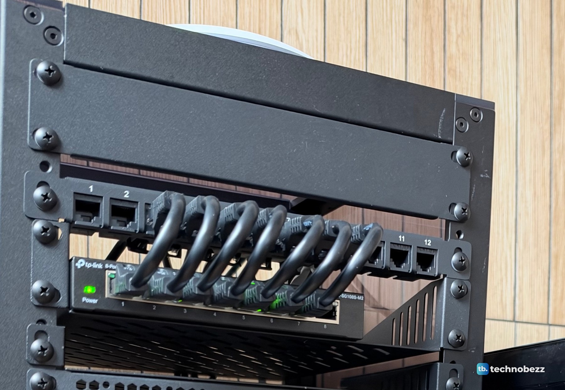 A 12-port patch panel with short black jumpers looping down into a TP-Link 2.5G switch inside the 10-inch rack
