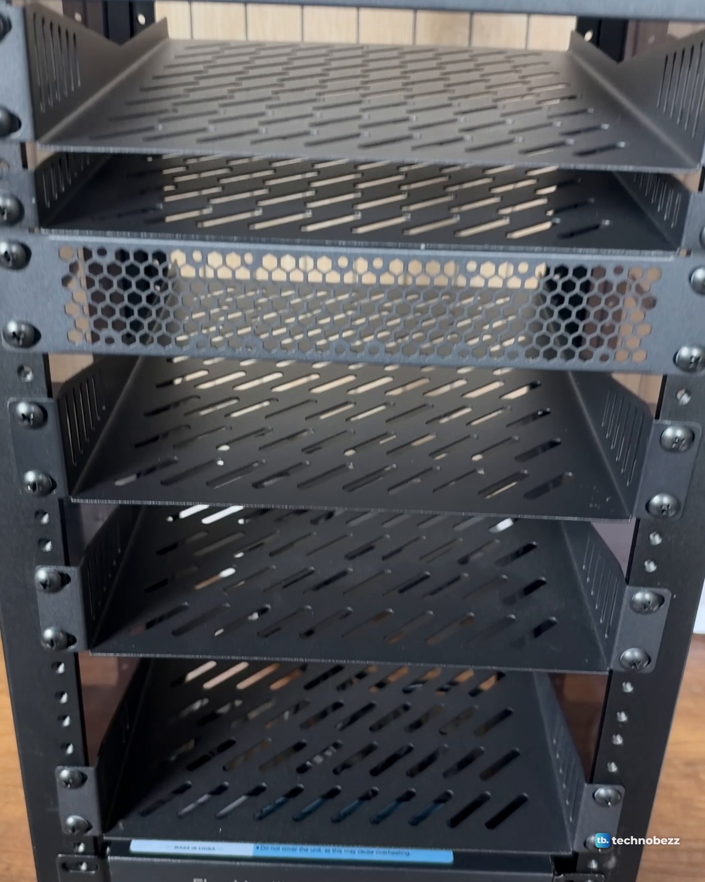 Close view of black perforated 1U shelves stacked in the empty 10-inch rack, with a vented blank panel between them