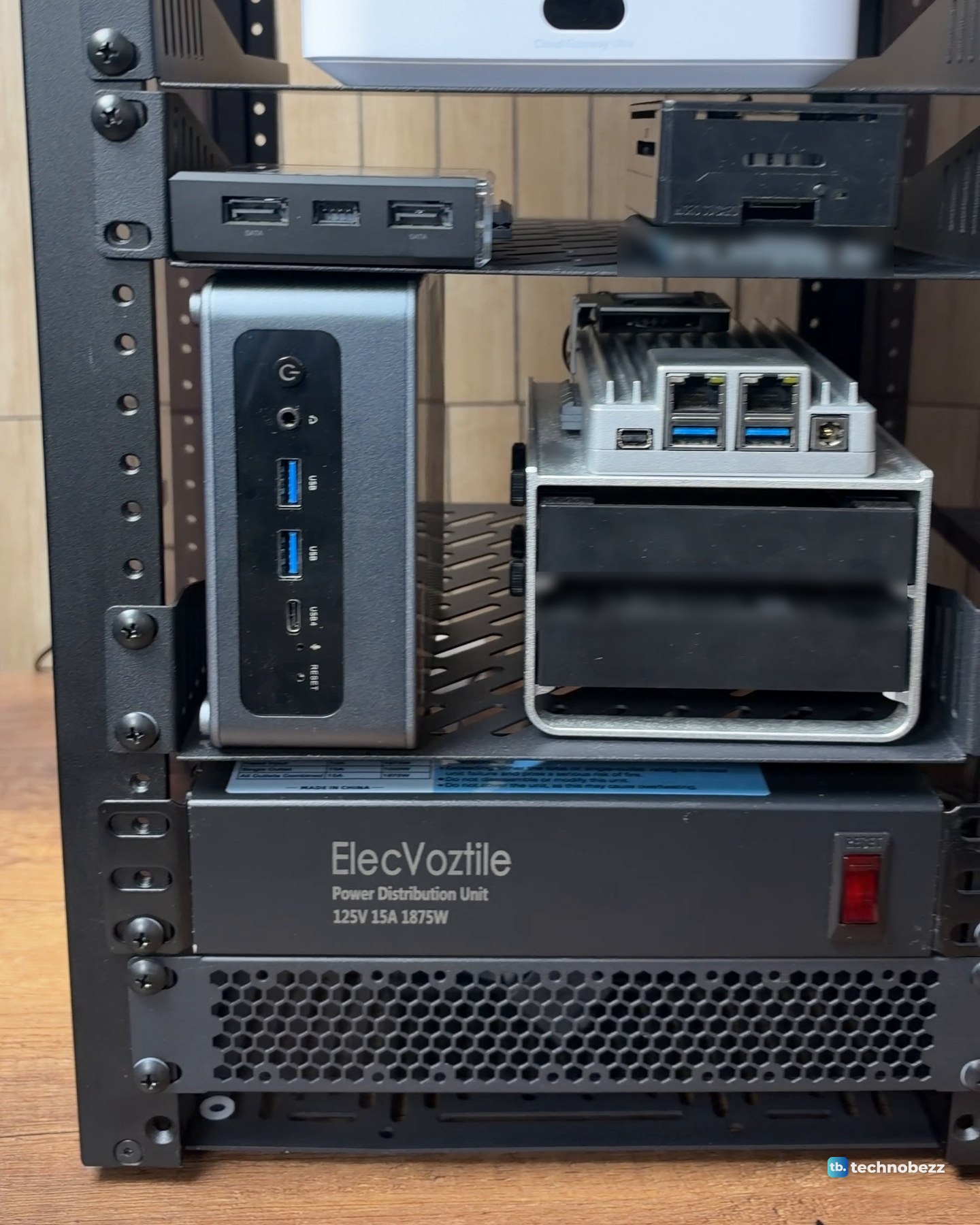 A grey ACEMAGIC F5A mini PC and a silver ZimaBoard 2 side by side on a black 1U shelf, with a rack power strip below