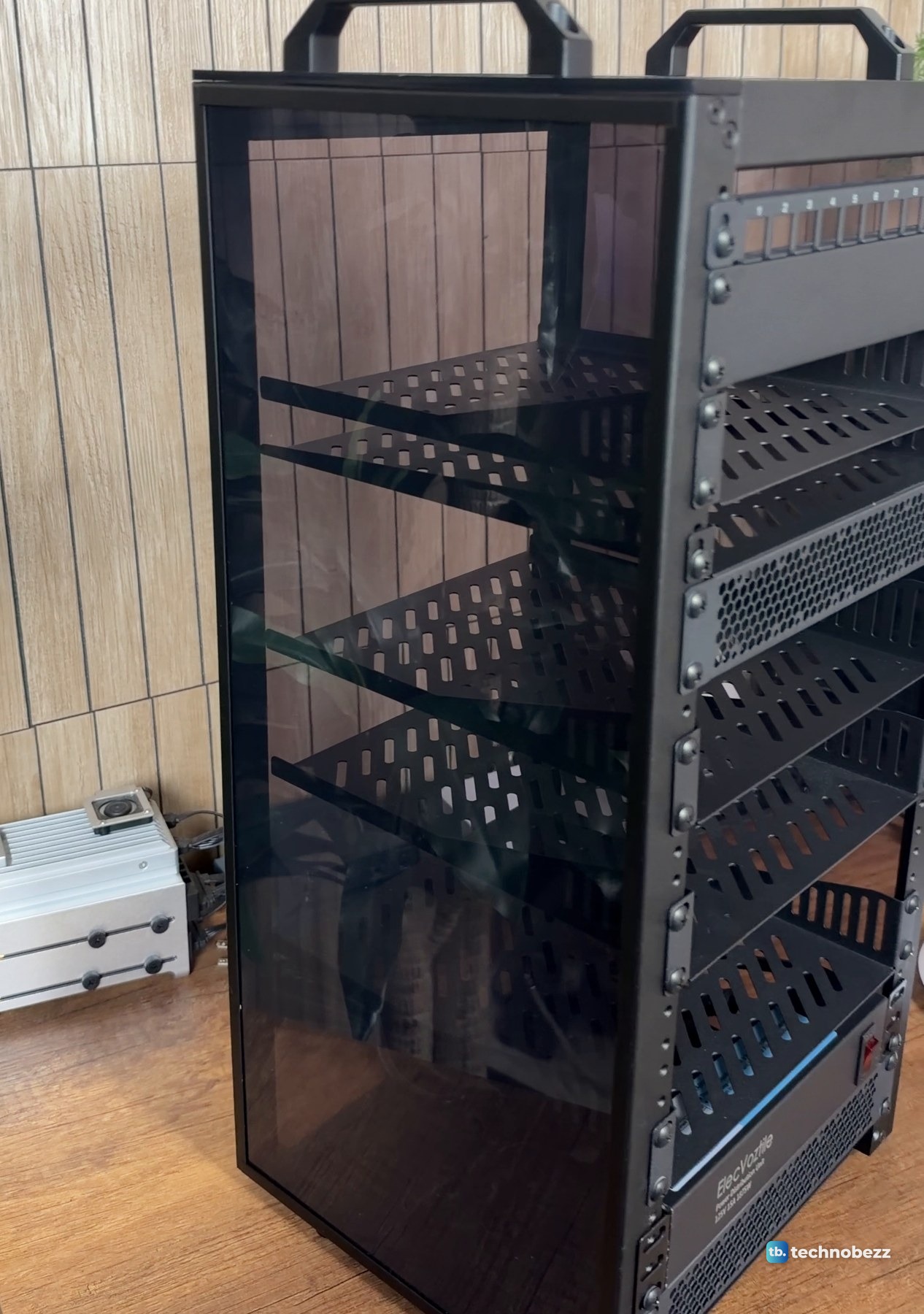 The empty DeskPi RackMate T2 from the side, showing the smoked acrylic panel, vented shelves and two carry handles