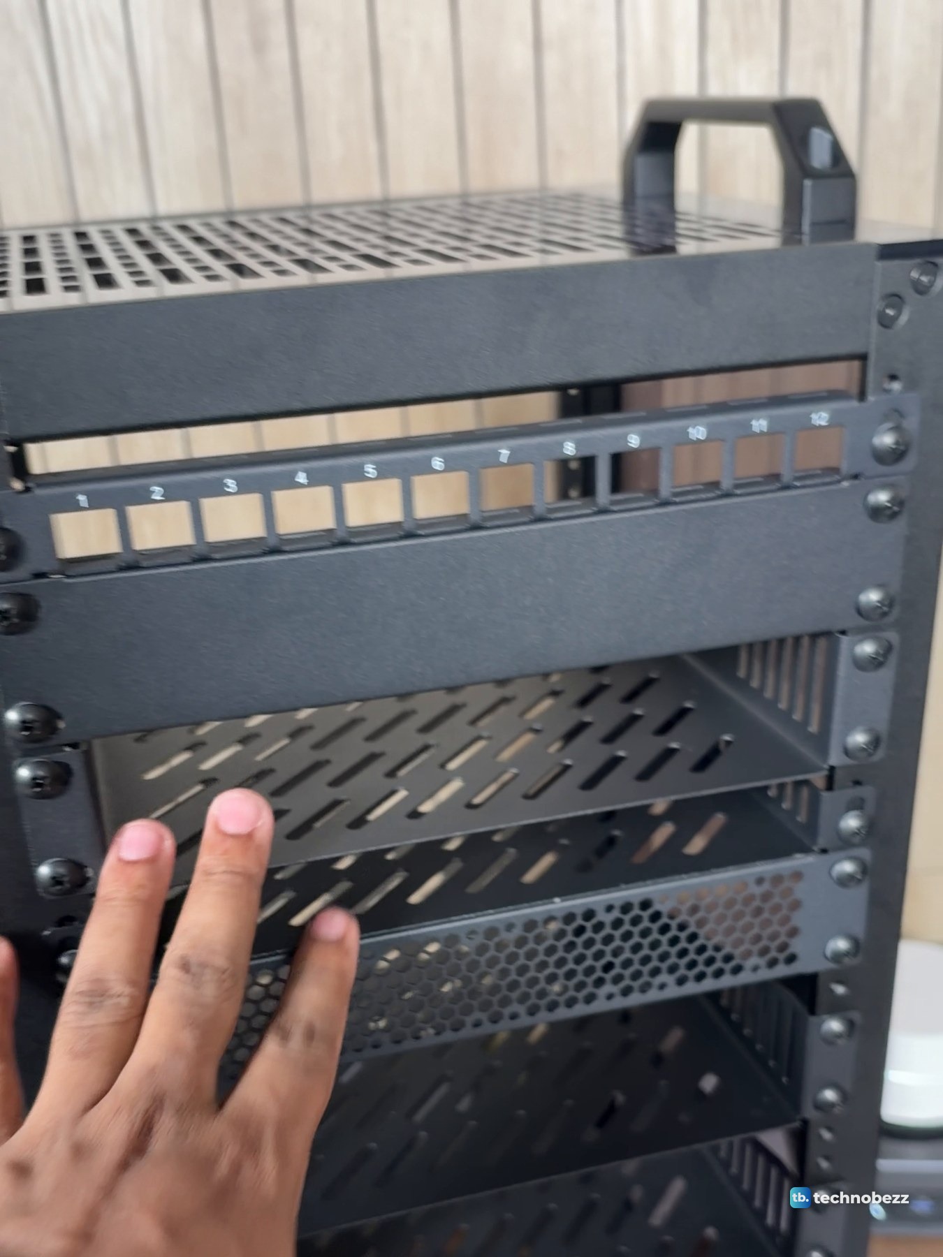 A hand held up to the empty shelves of the DeskPi RackMate T2 under the patch panel