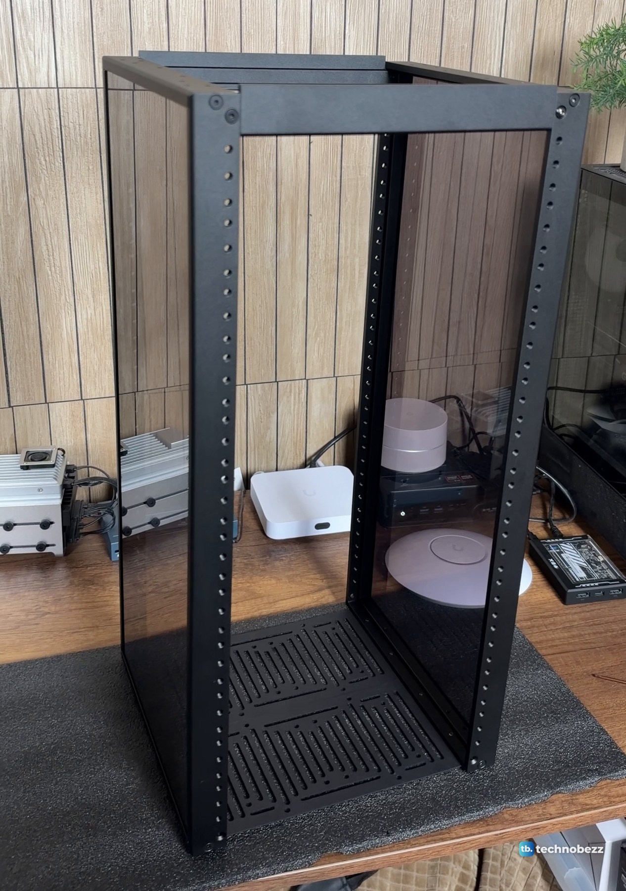 The DeskPi RackMate T2 frame with both smoked side panels fitted, standing open-topped on a foam sheet on the desk