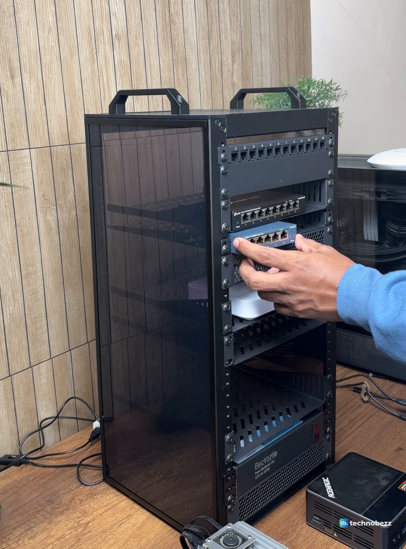 A hand sliding a small blue network switch onto a shelf inside the DeskPi RackMate T2