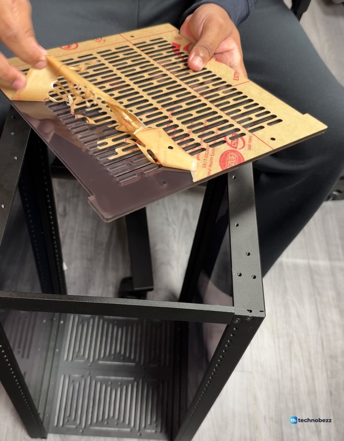 Brown protective paper being peeled off a vented plate held above the DeskPi RackMate T2 frame