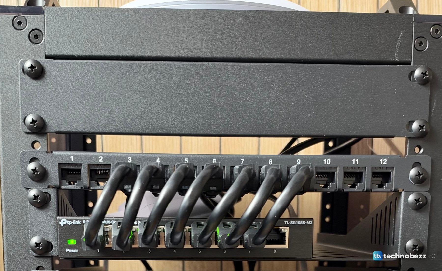 Front of the rack top with a blank panel, a 12-port patch panel and a TP-Link 2.5G switch below it, short black jumpers looping between them