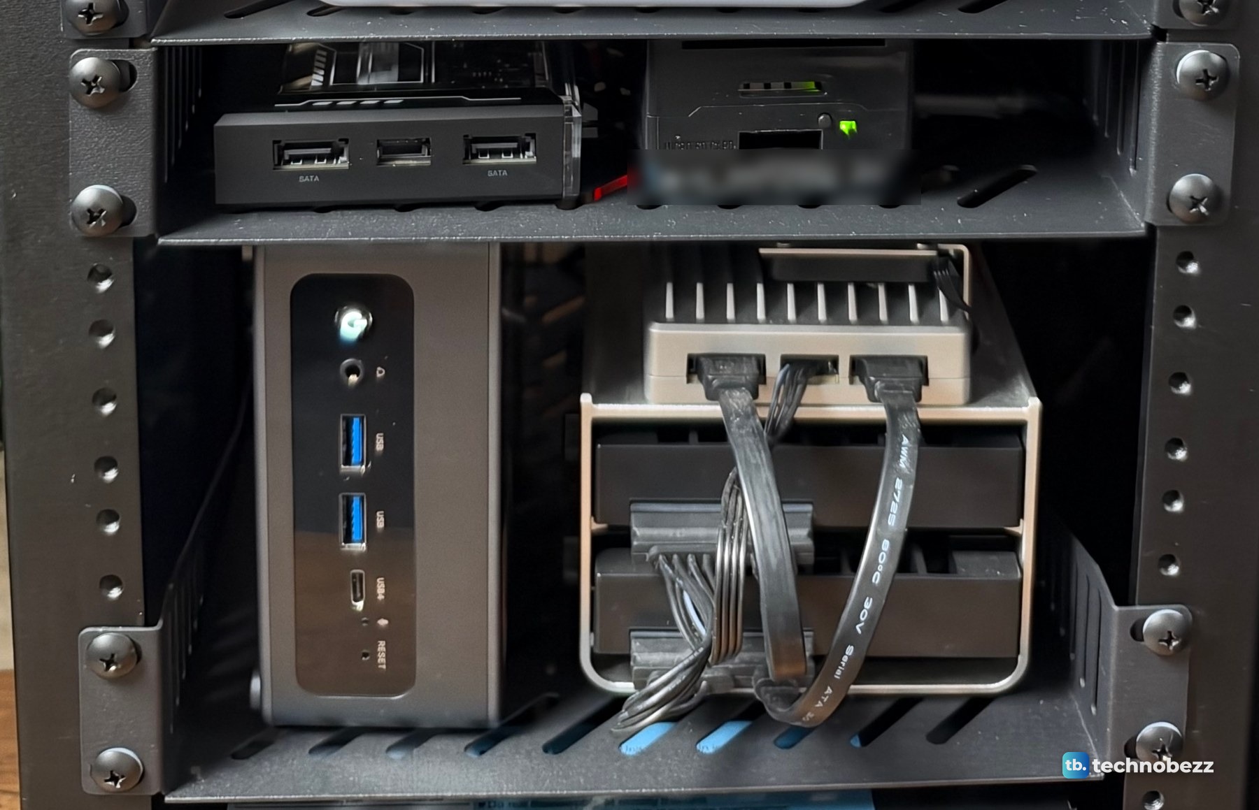 Two rack shelves with small computers, the upper one with two small boards and the lower one with a grey mini PC standing on its side next to a silver finned board