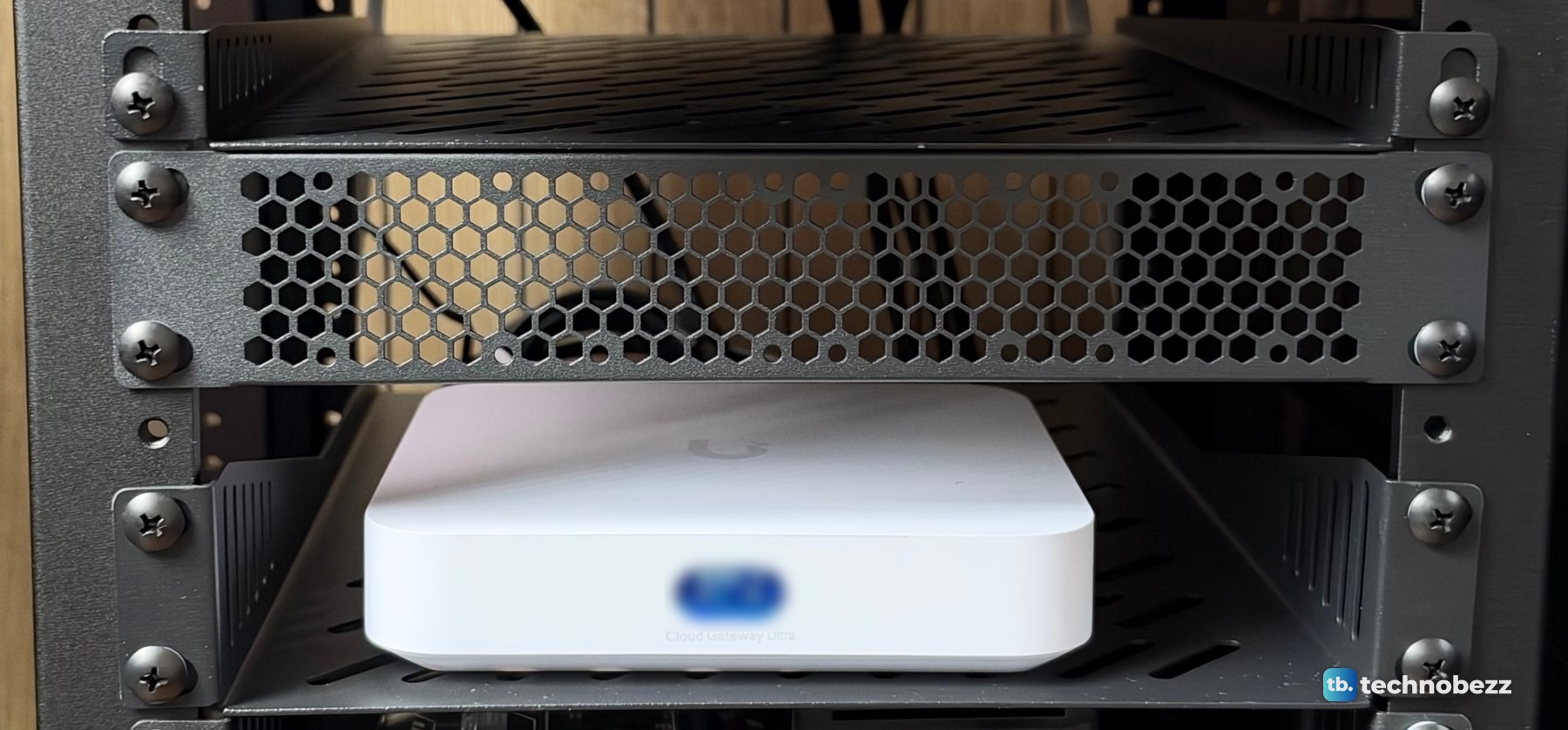 A black vented rack panel above a white UniFi Cloud Gateway Ultra sitting on a 1U shelf