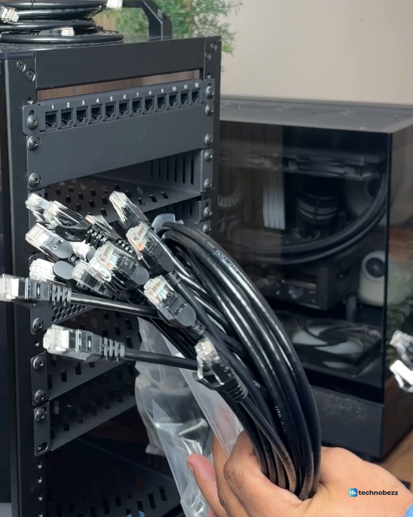 A hand holding a bundle of black Cat6 patch cables in a plastic bag in front of the empty rack