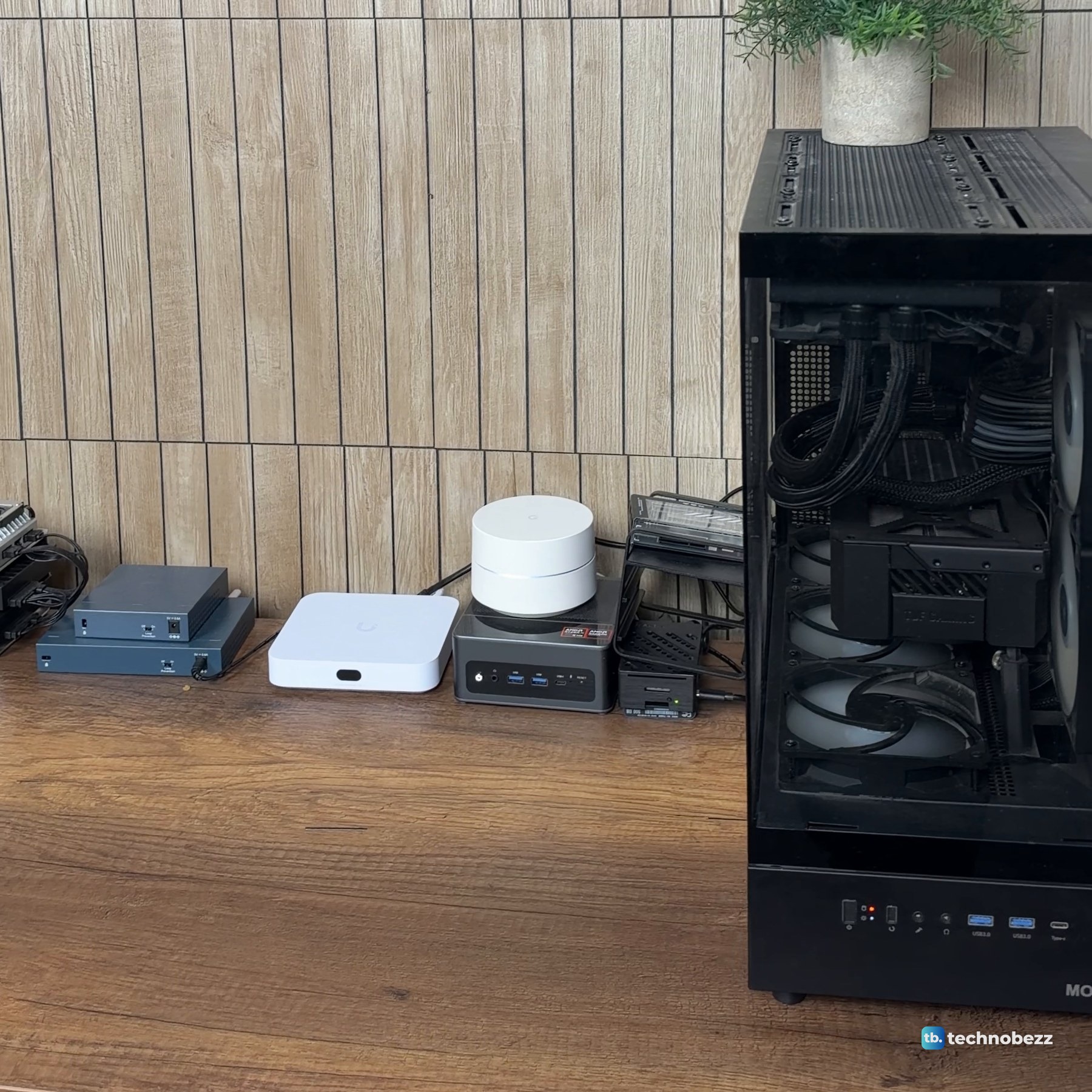 Small computers, a switch, the white UniFi gateway and a Wi-Fi puck in a row on the wood desk, with the tower PC at the right