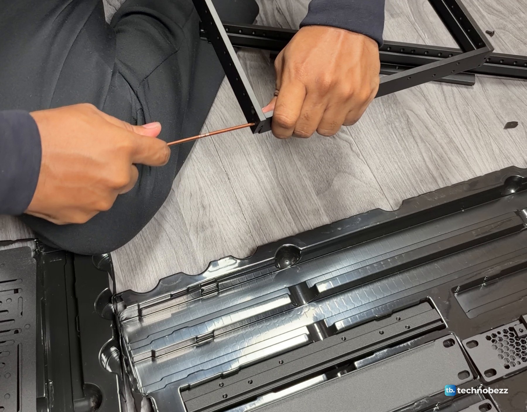 Hands tightening a corner joint of a DeskPi RackMate T2 side frame on the floor