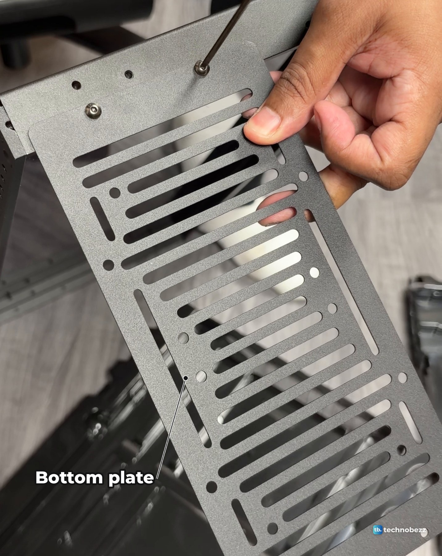 A vented metal bottom plate held against the DeskPi RackMate T2 frame while a screw goes in
