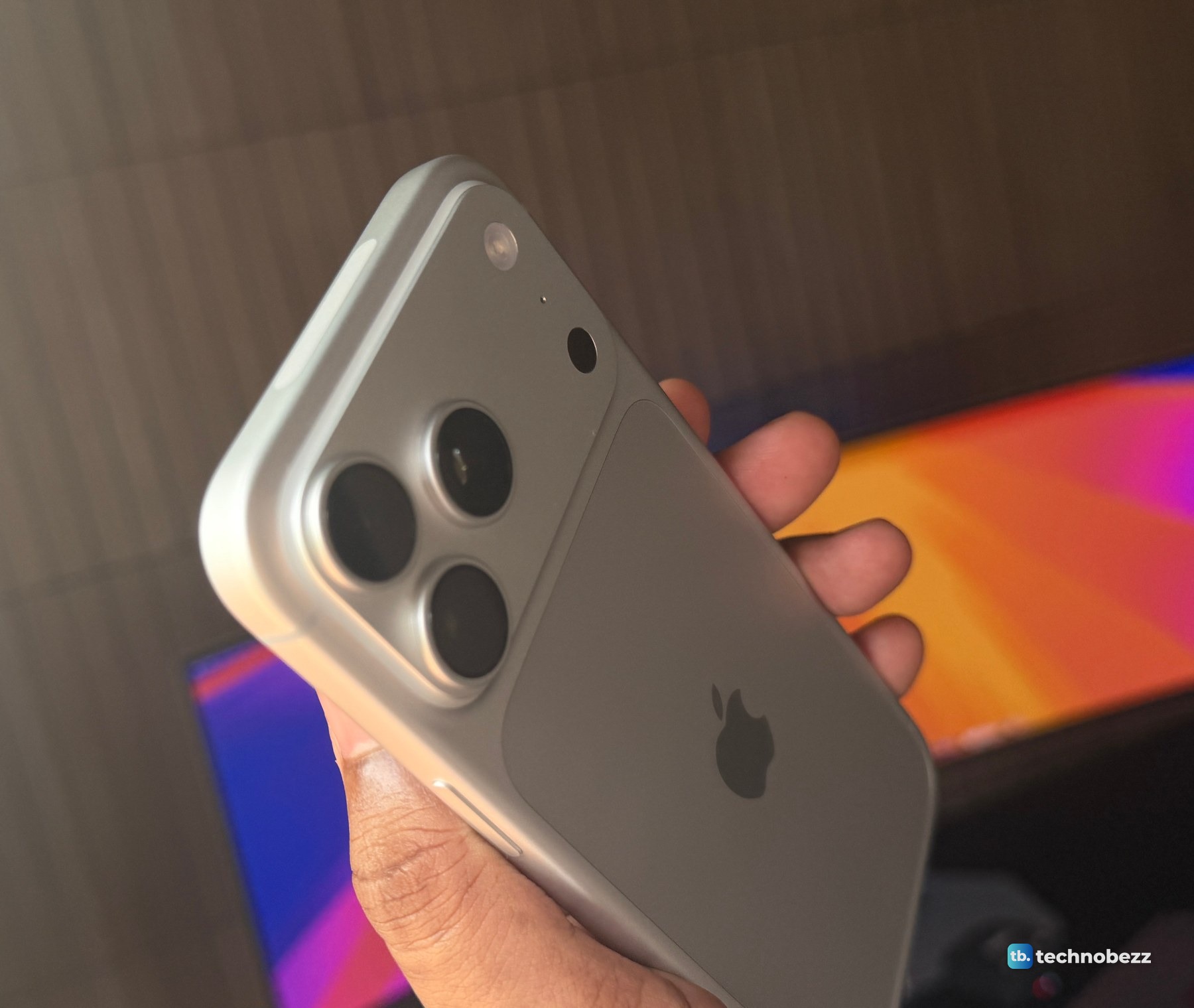 Silver iPhone 18 Pro Max held in one hand, showing the three rear camera lenses