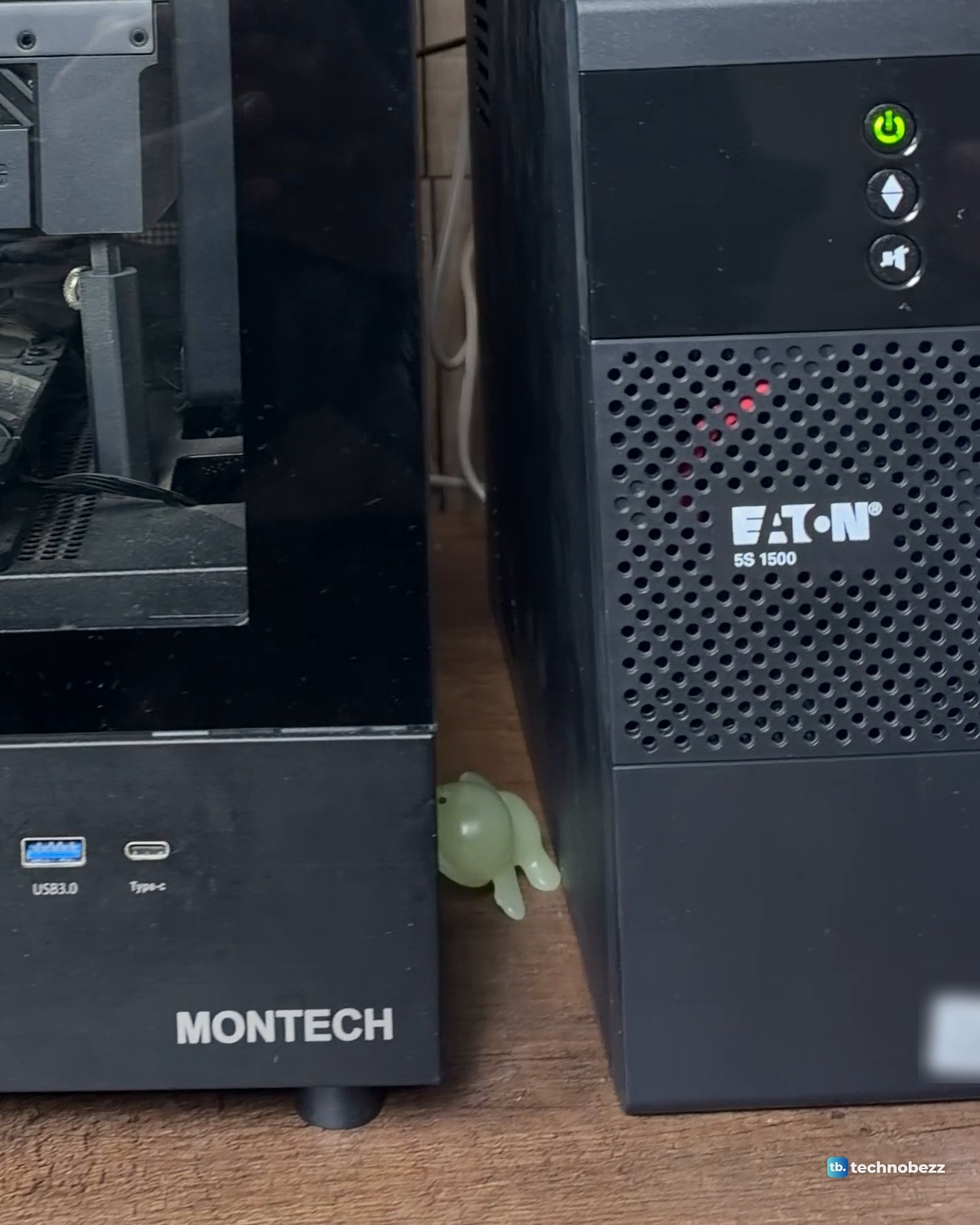 Black Eaton 5S 1500 tower UPS with a green power light standing on a wood desk next to a black MONTECH tower PC