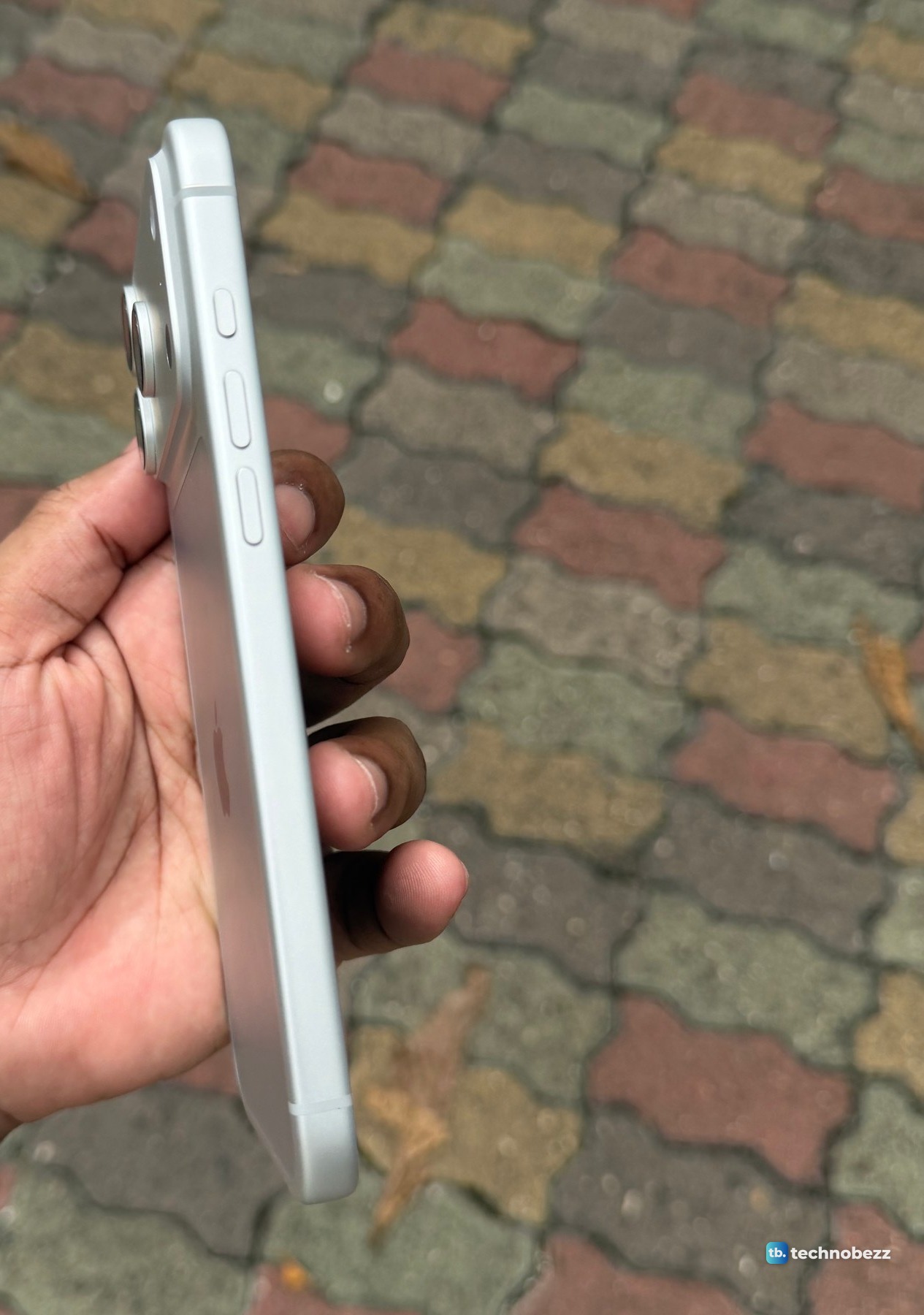 Left edge of a silver iPhone 18 Pro Max held in a hand, showing one short button above two longer buttons