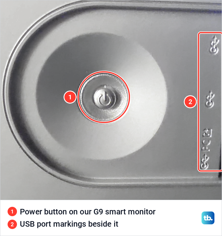 Close-up of a round metal power button in a recess on our Samsung smart monitor, beside USB port markings.