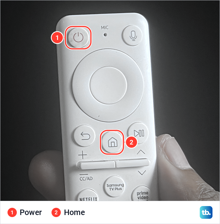 A hand holding a white Samsung remote with the Power and Home buttons marked.