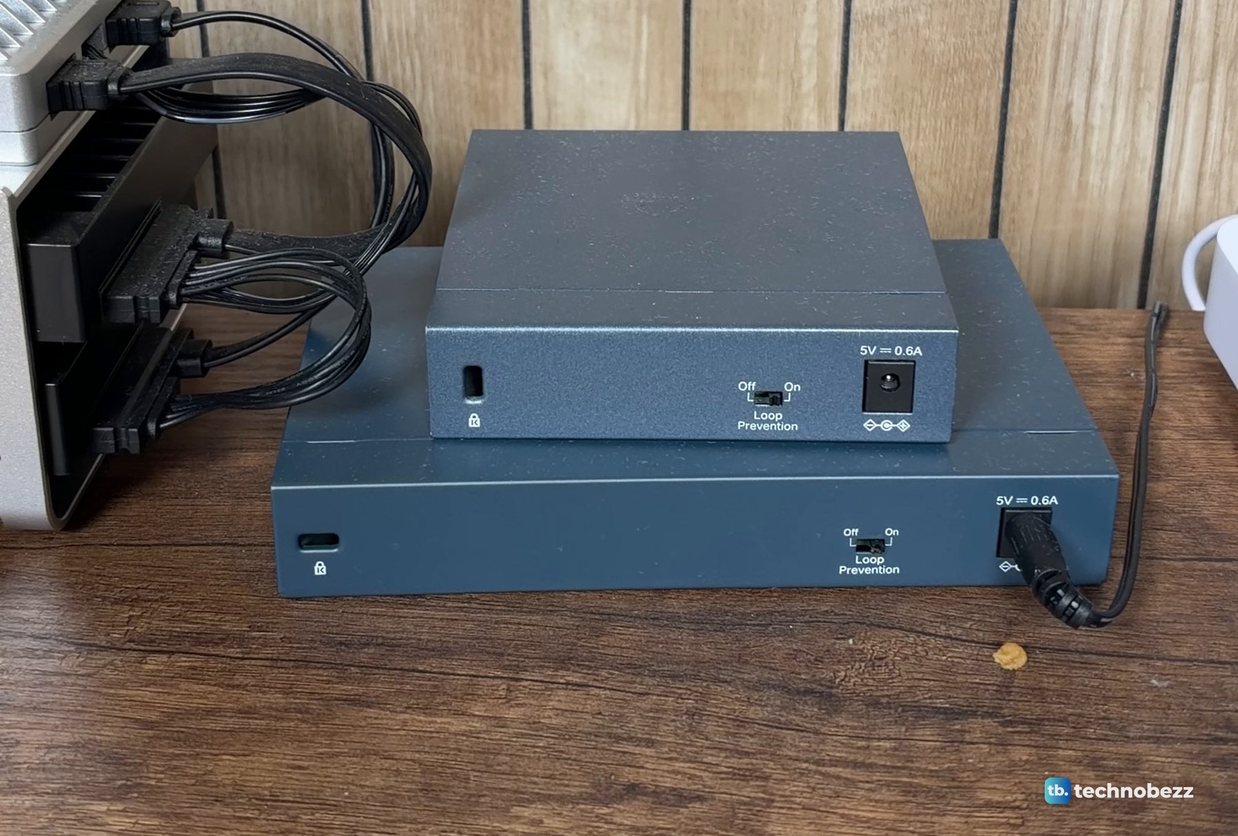 Two blue-grey network switches stacked on a wood desk with a bundle of black cables beside them