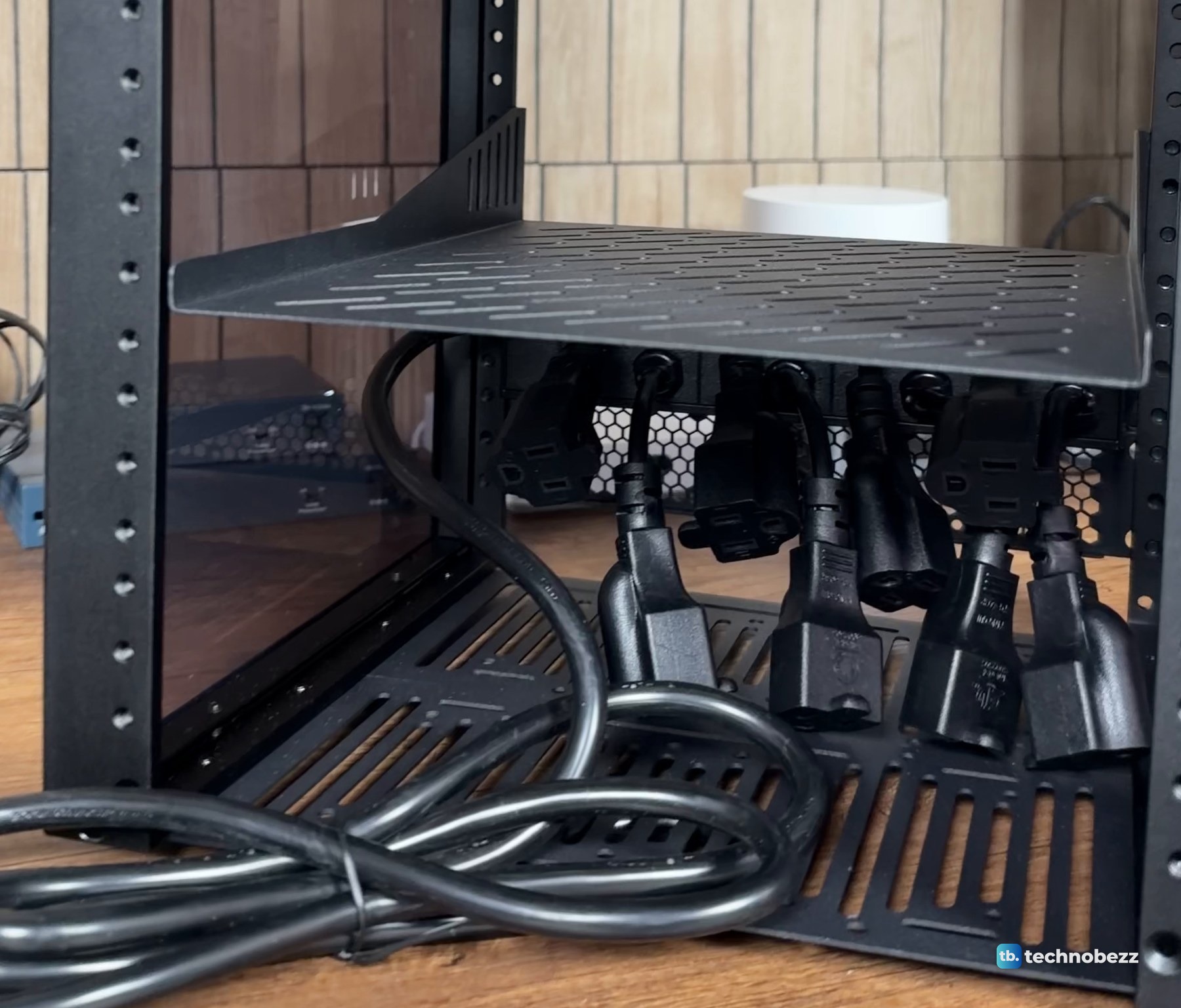 Back of a rack power strip with short outlet leads hanging under a shelf and a coiled power cord on the bottom shelf