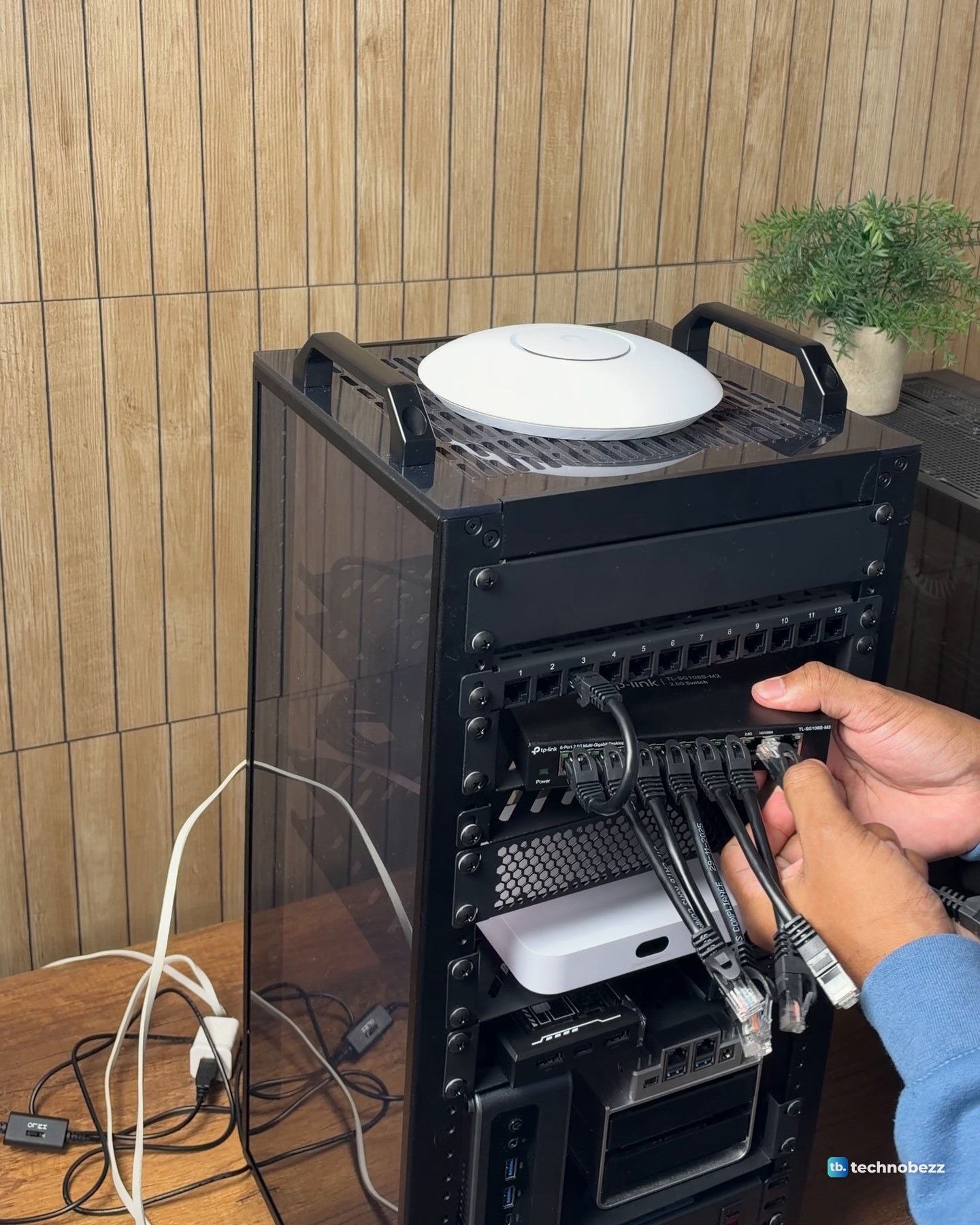 A hand plugging a short black patch cable into the TP-Link 2.5G switch under the patch panel, with the U7 Lite sitting on top of the rack