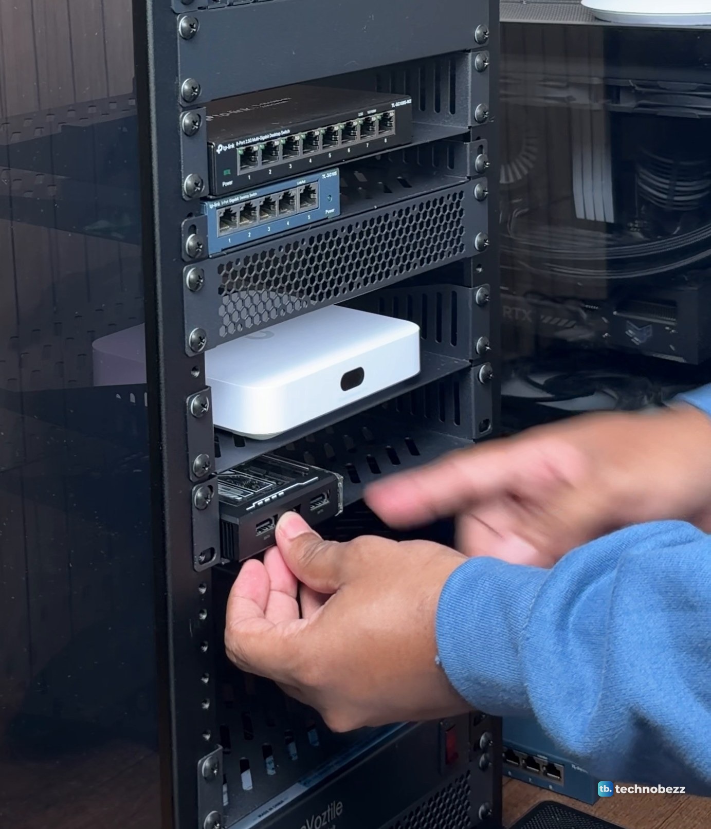Hand sliding a ZimaBlade onto a 1U rack shelf below a white UniFi Cloud Gateway Ultra