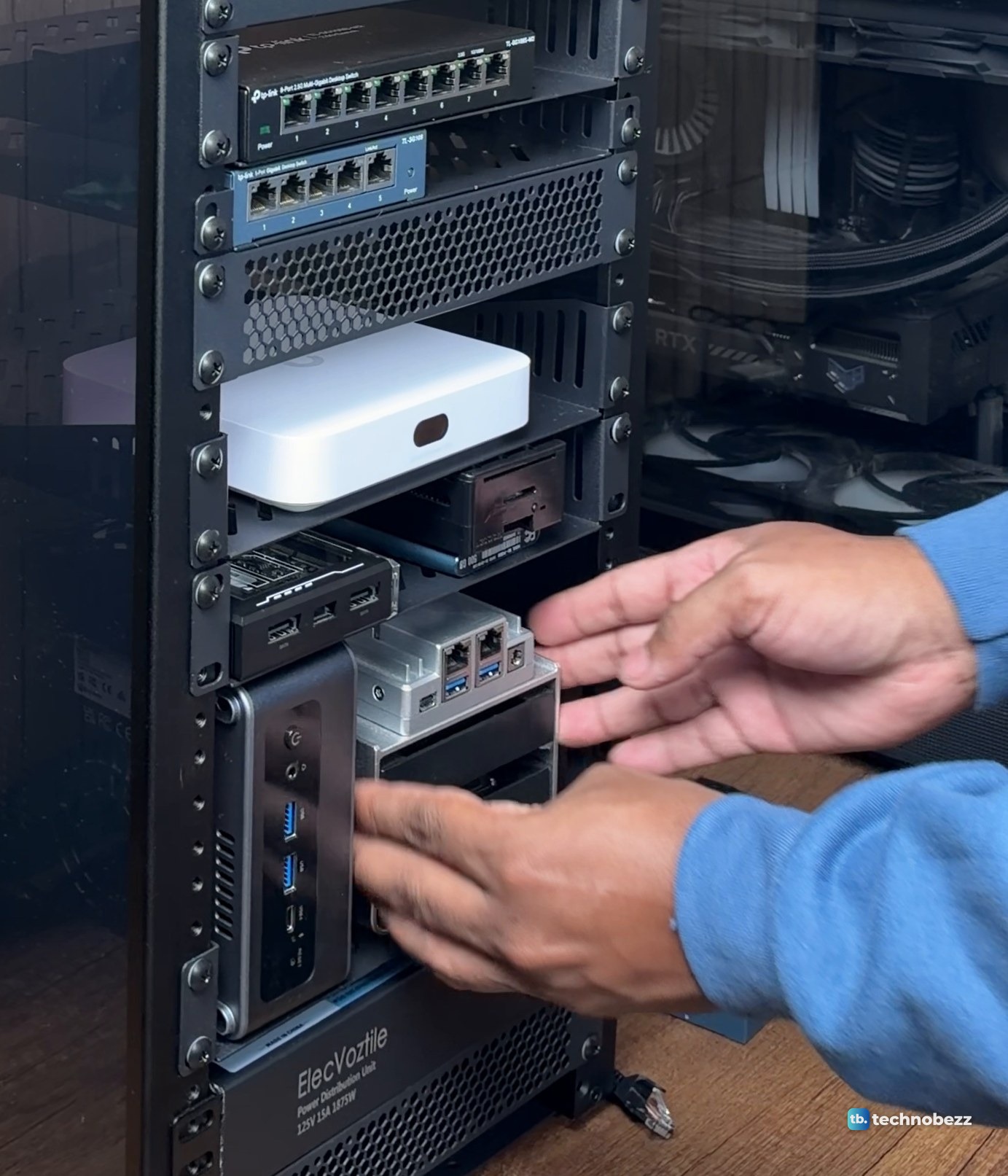 Two hands sliding a ZimaBoard 2 on its drive frame onto the rack shelf beside the ACEMAGIC F5A