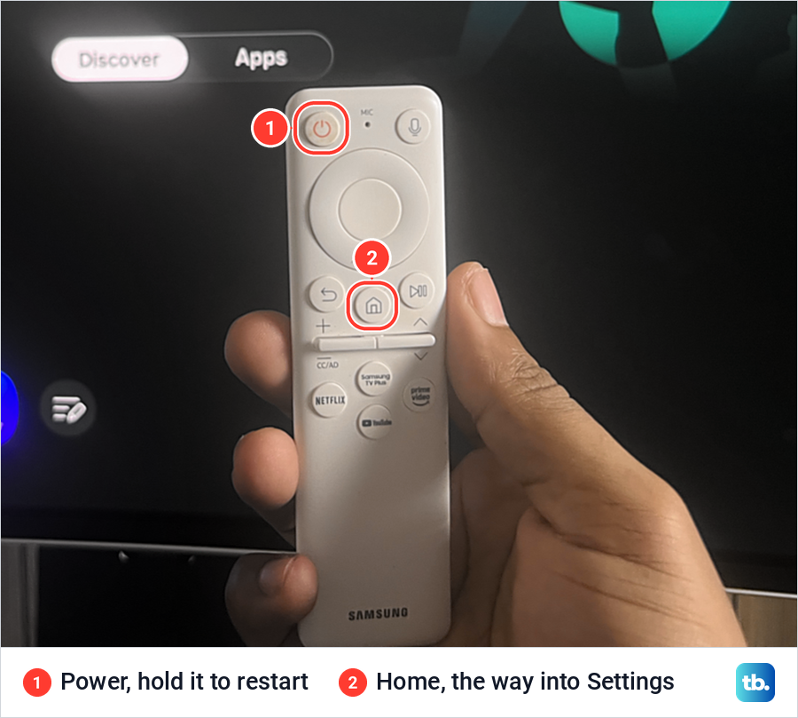 A hand holding a white Samsung remote in front of a Smart Hub screen, with the Power and Home buttons marked.