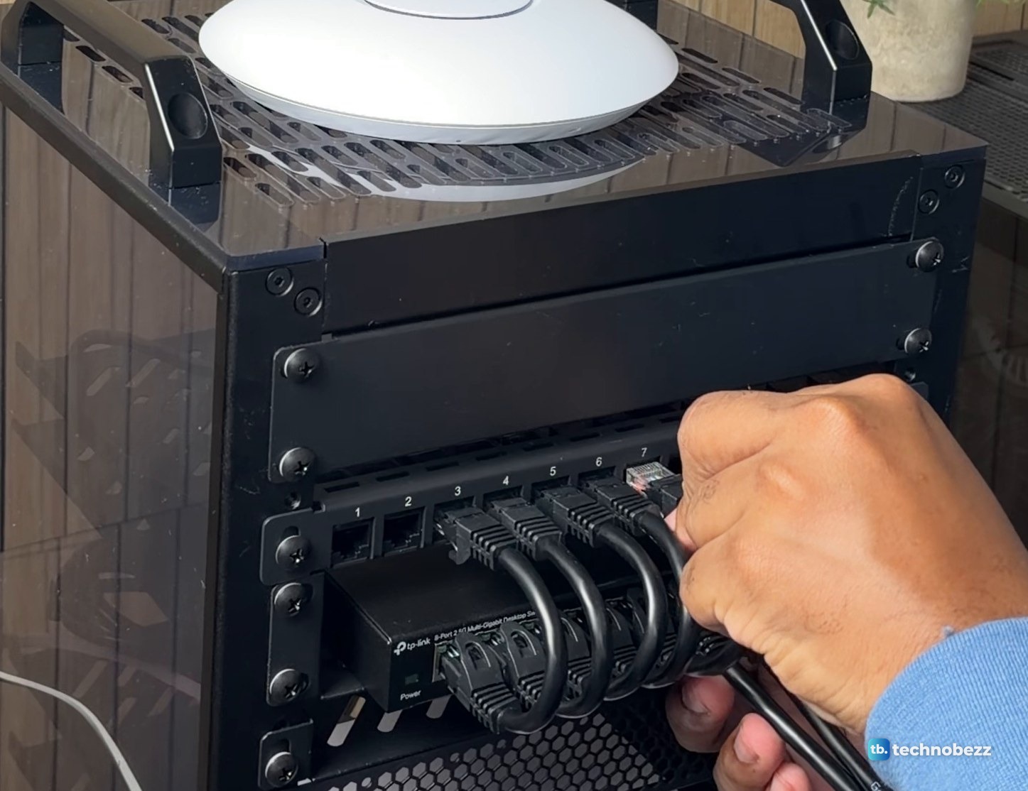 Hand pushing a short patch cable into a front port of the patch panel above a row of looped jumpers