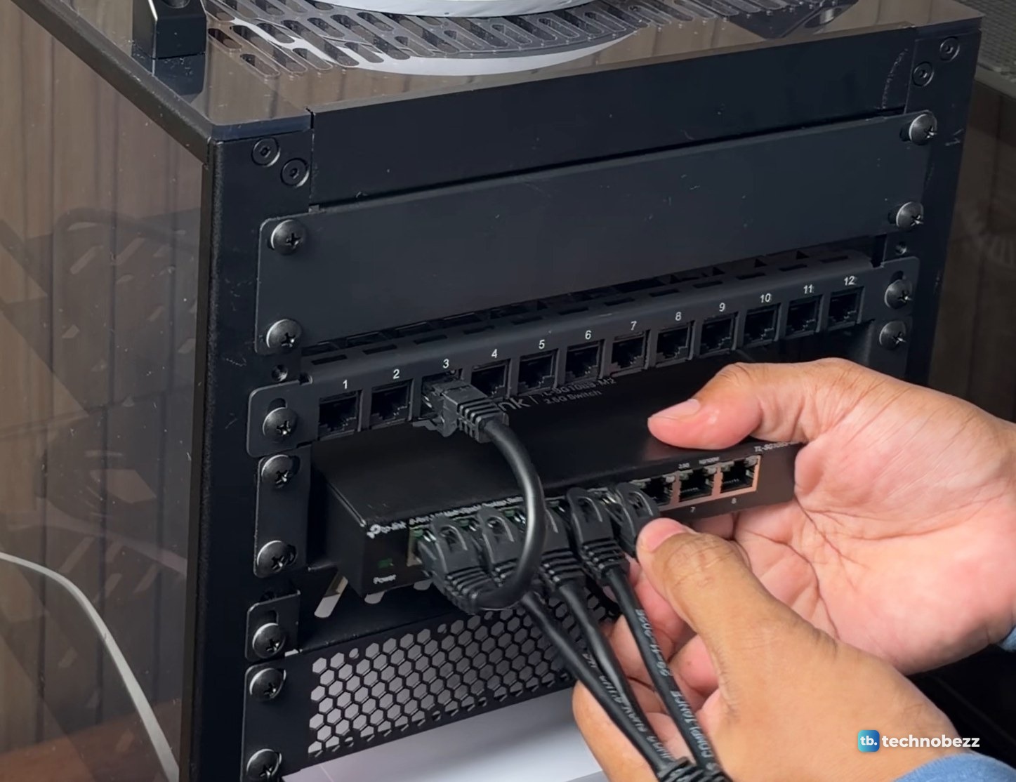 Hand pressing a short black patch cable into a port on a TP-Link 8-port 2.5G switch