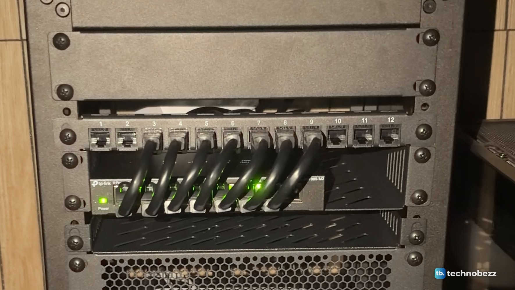 Green link lights on a TP-Link switch under a patch panel in a dim room