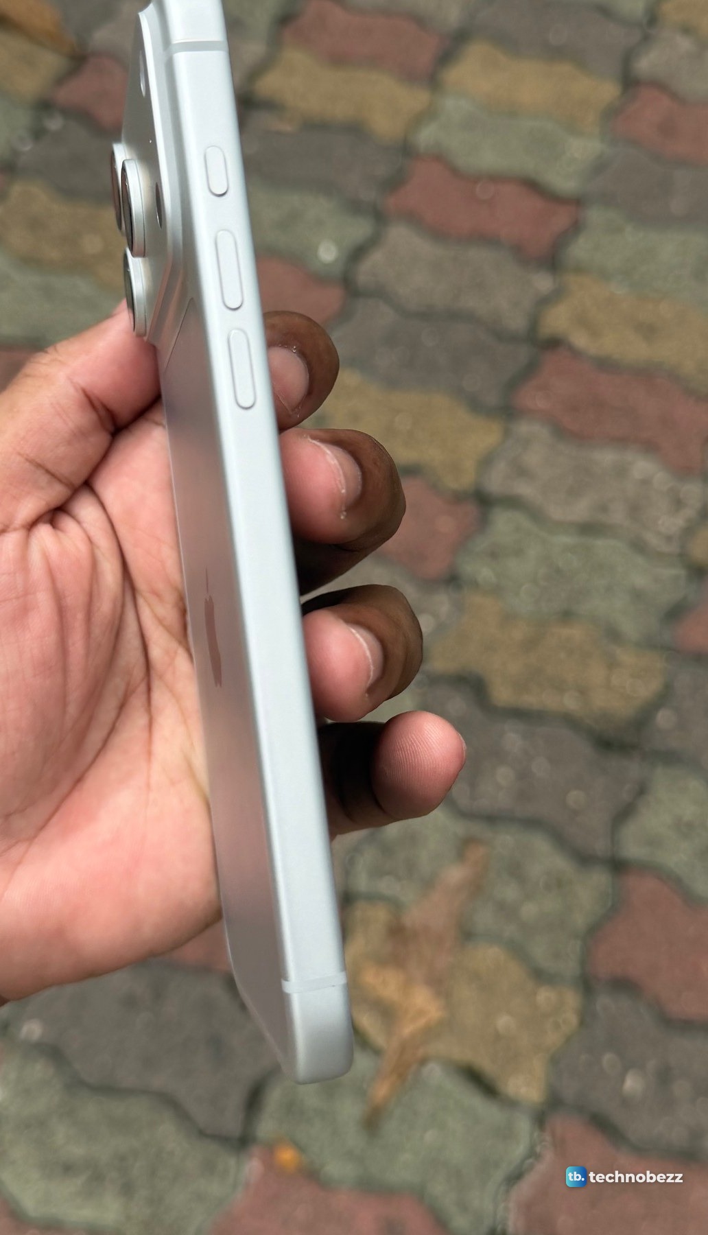 The left side of a silver iPhone 18 Pro Max held in a hand, showing the small Action button above the two volume buttons