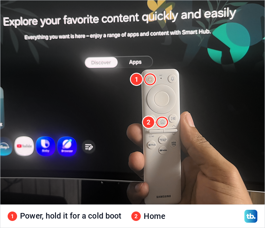 A hand holding a white Samsung remote in front of the Smart Hub screen, with the Power and Home buttons marked.