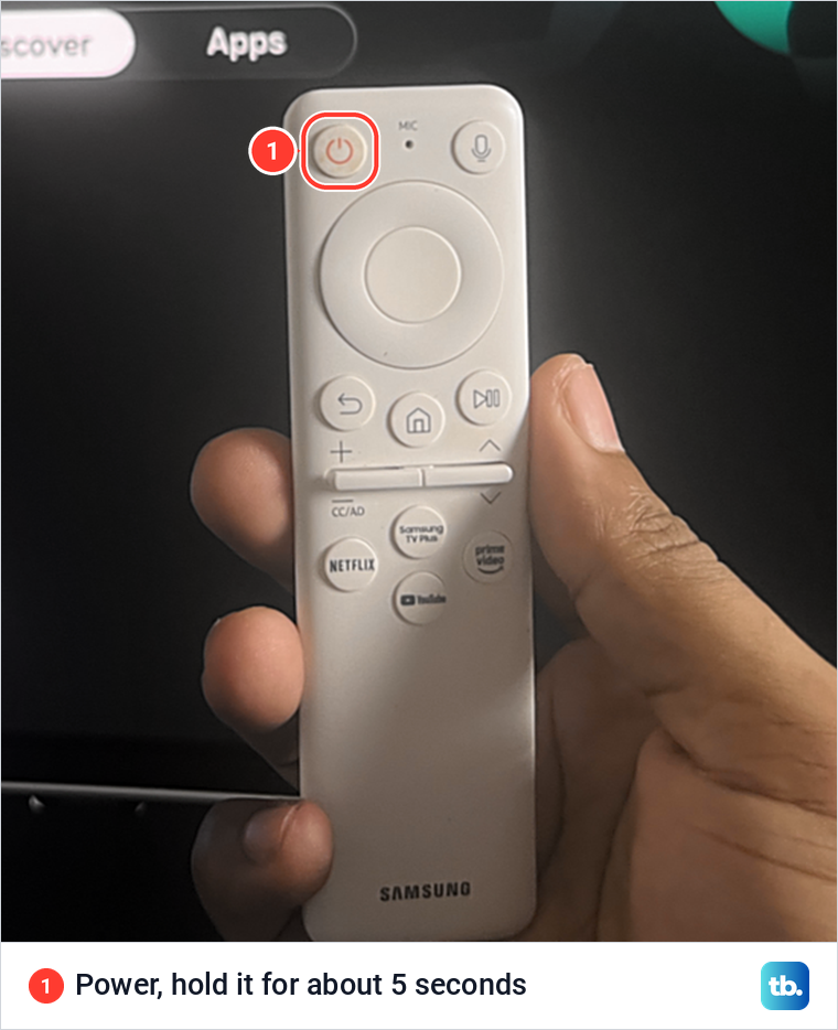 A hand holding a white Samsung remote with the Power button at the top left circled.