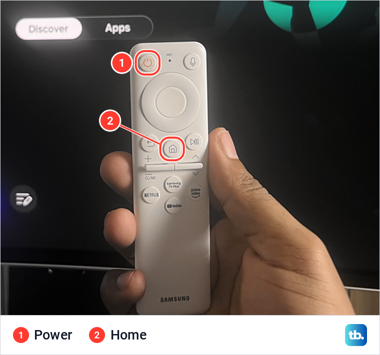 A hand holding a white Samsung remote with the Power key and the Home key marked.