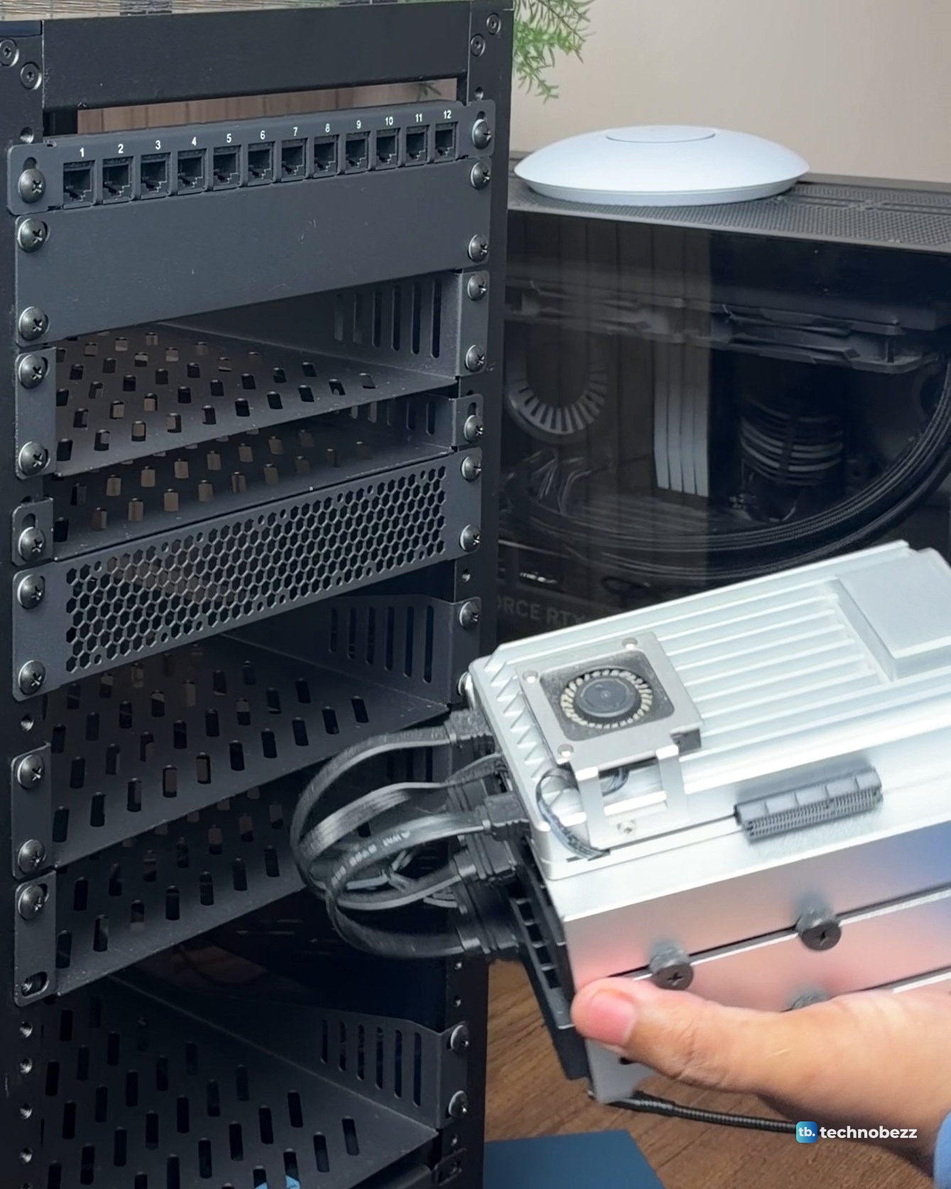 A hand holding the silver finned ZimaBoard 2 with cables attached, in front of the empty rack shelves