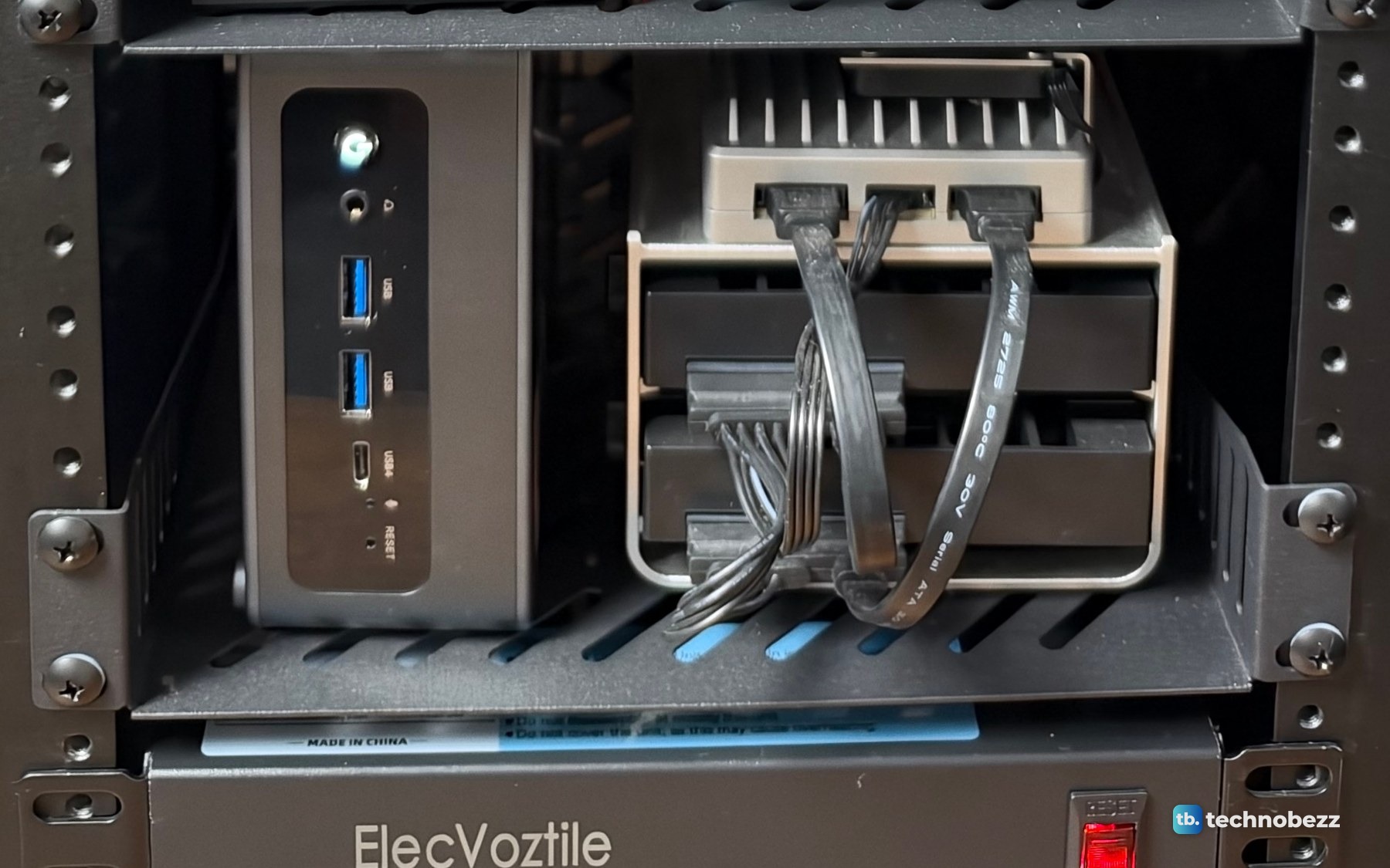 The ACEMAGIC F5A standing upright on the left of a shelf, and the silver ZimaBoard 2 on its drive frame on the right