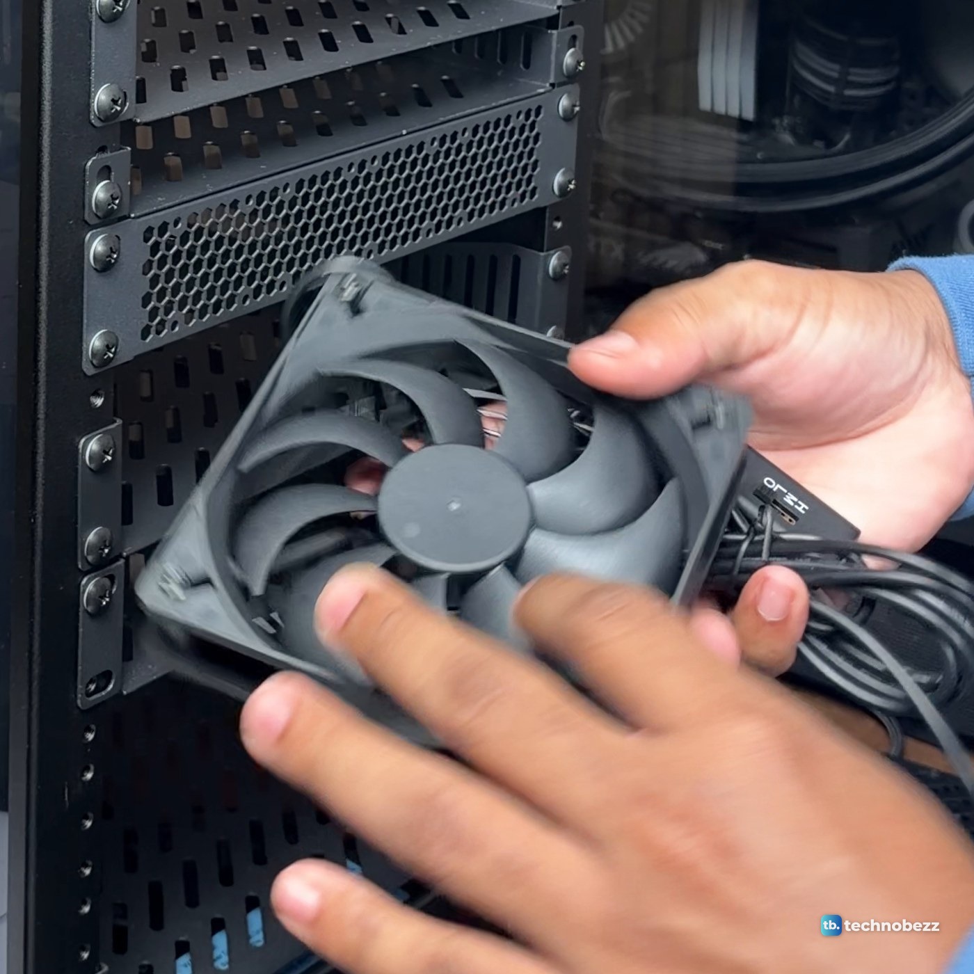 Hands holding a black 120 mm fan with its USB cable in front of the rack