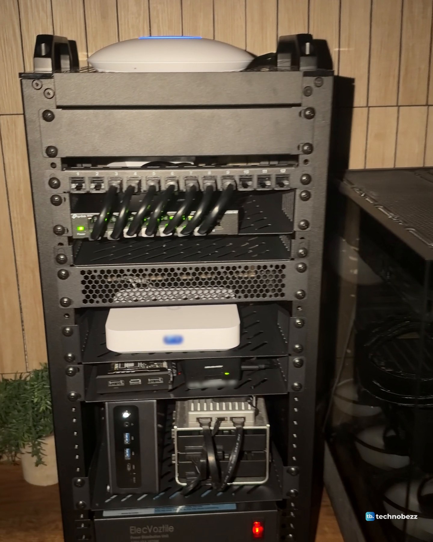 The rack in a dim room with the U7 Lite ring glowing blue, green lights on the switch and the red power switch lit