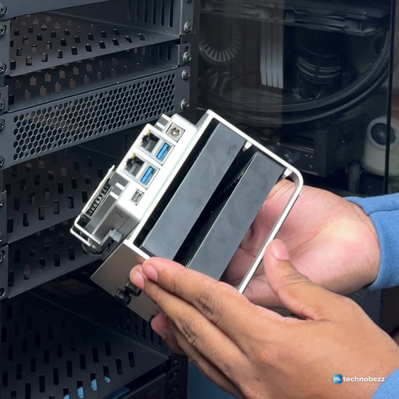 Hands holding the ZimaBoard 2 with its Ethernet and USB ports facing out, two drives in a silver frame under it