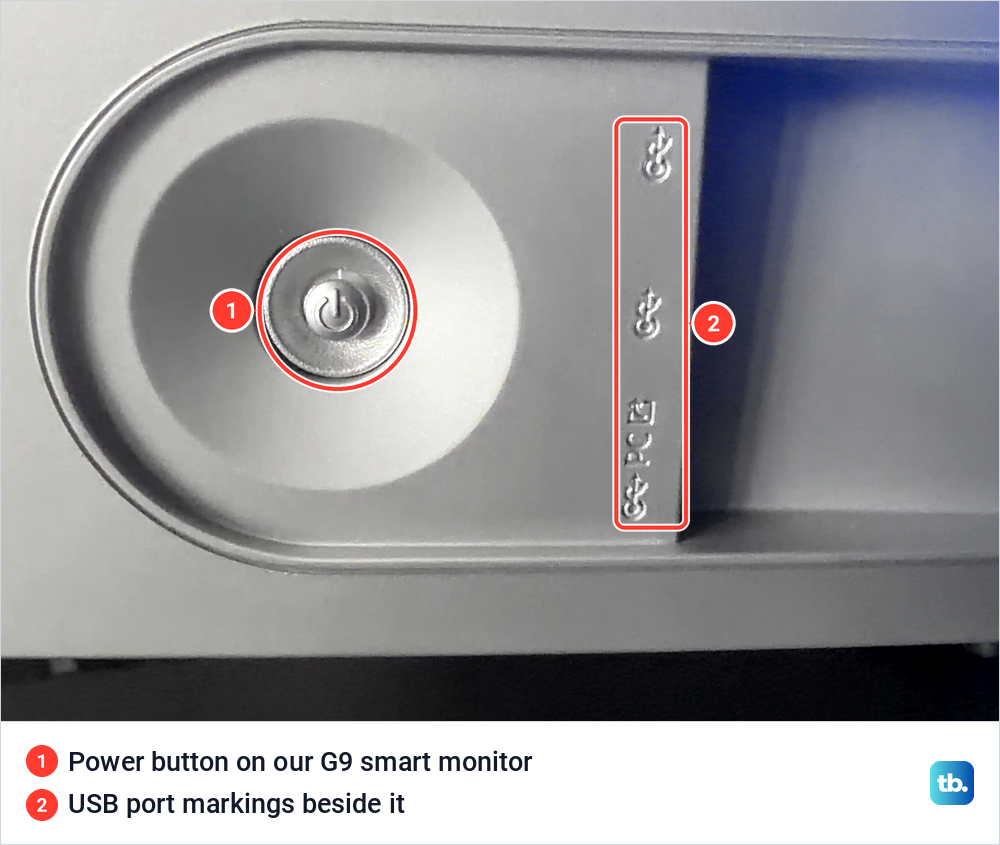 Round metal power button in a recess on our Samsung smart monitor, beside embossed USB port markings.