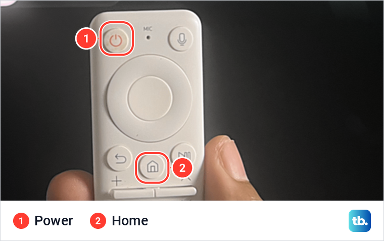 A hand holding a white Samsung remote with the Power and Home buttons marked.
