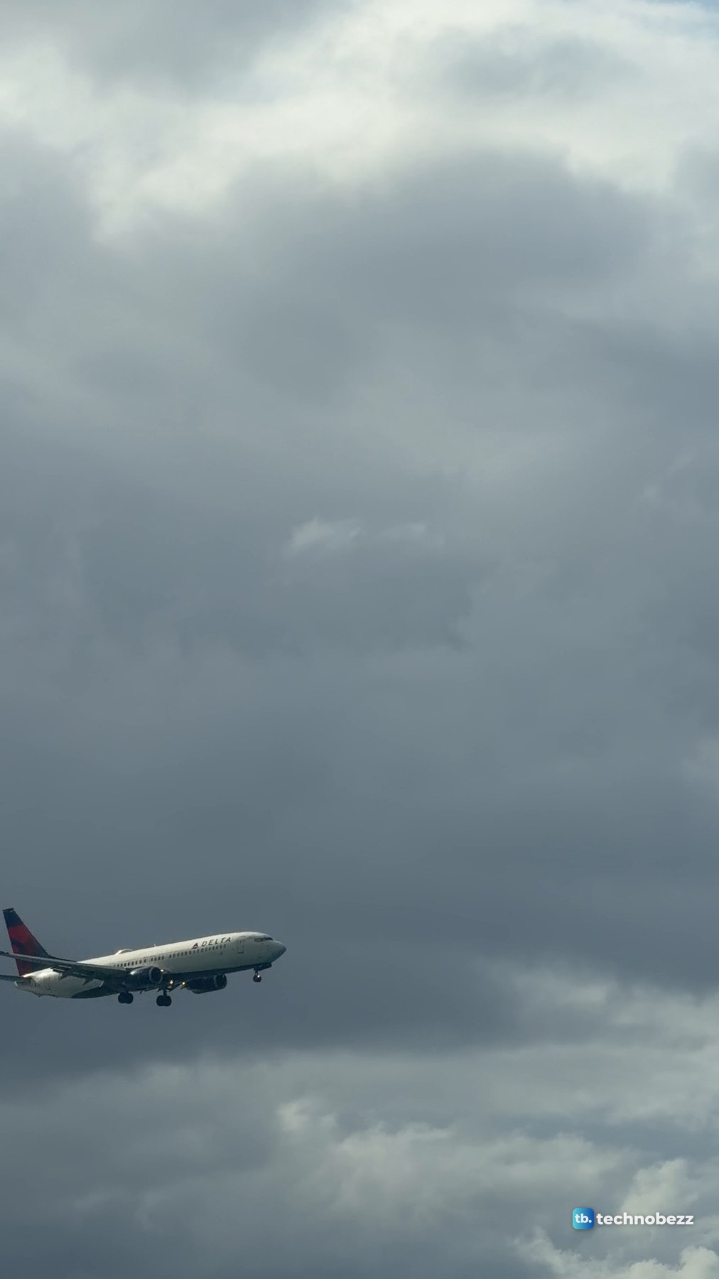 An airliner with its landing gear down in front of a dark storm cloud