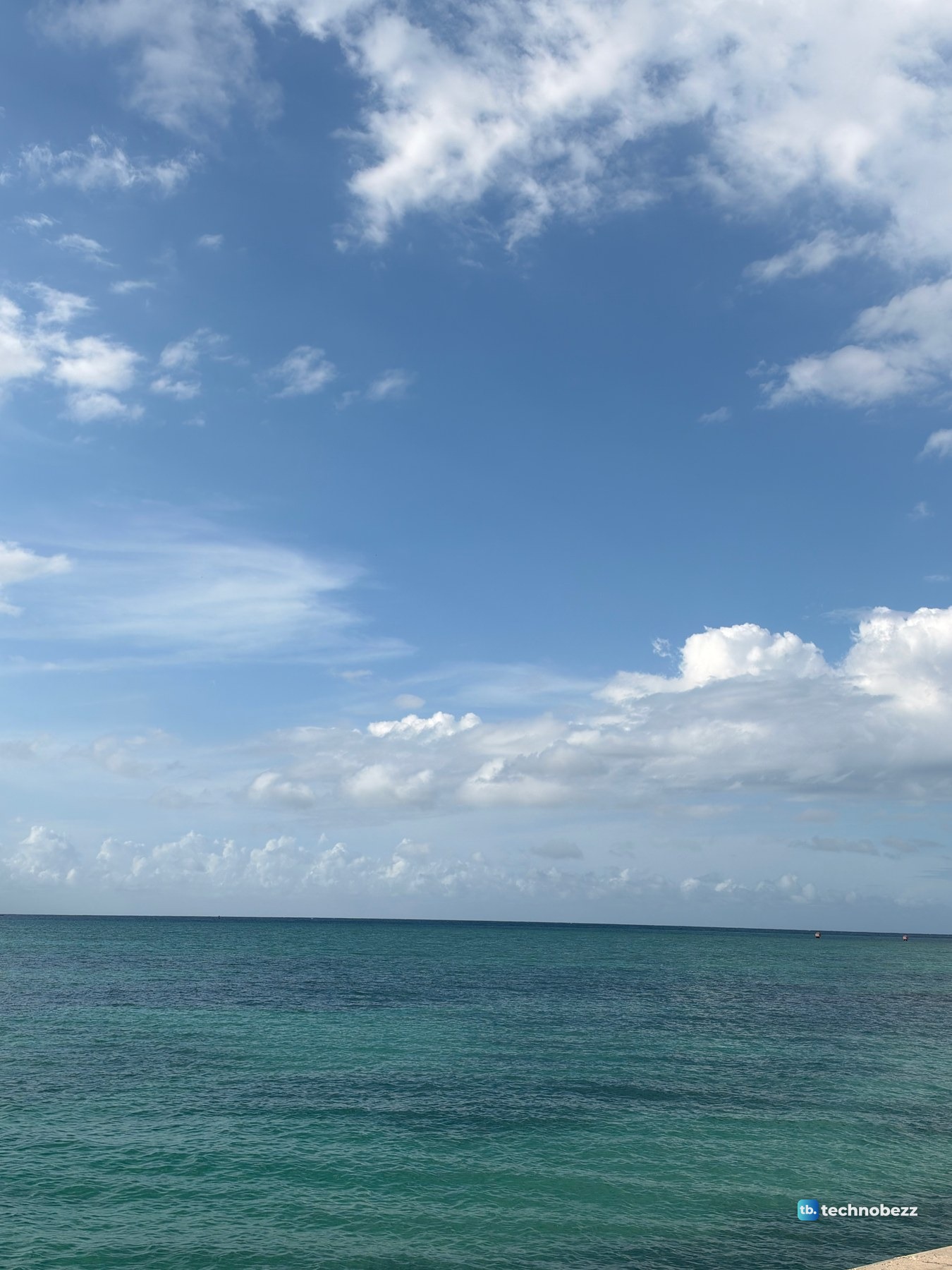 Teal sea under a mostly clear blue sky with white clouds near the horizon