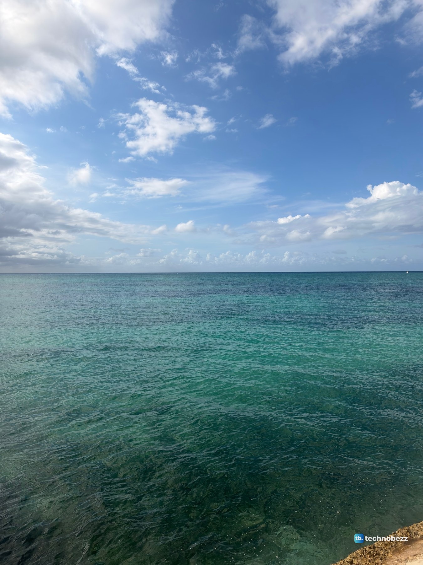 Teal sea under a blue sky with scattered white clouds