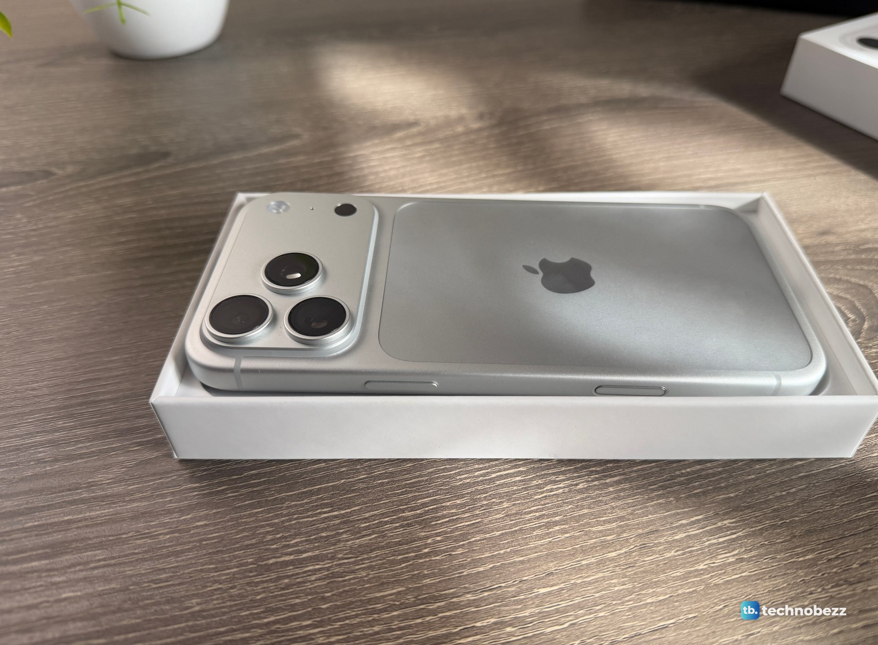Silver iPhone 18 Pro Max lying face down in its open box tray, with the camera bar nearest the lens