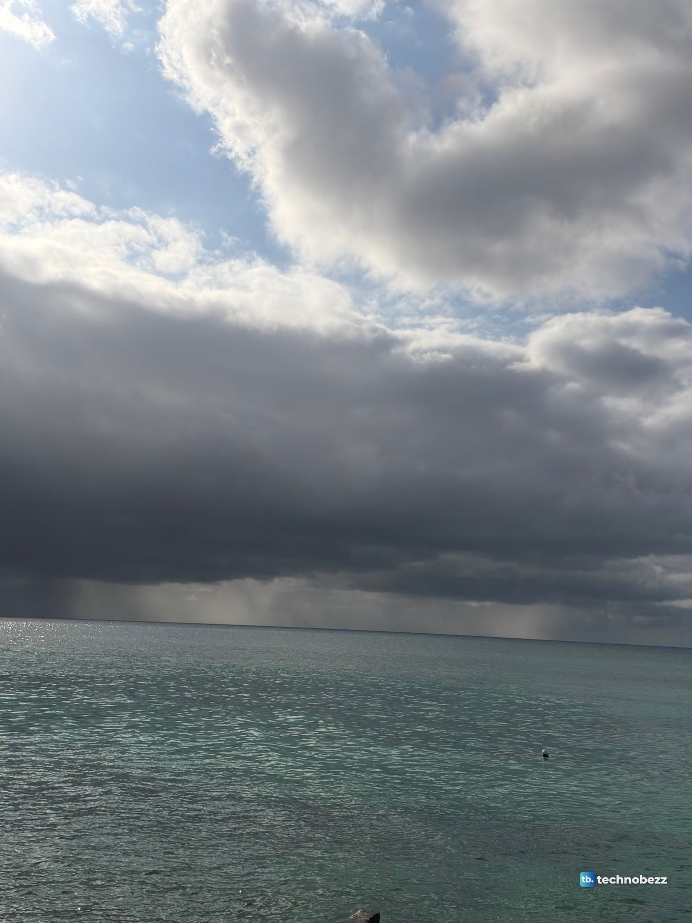 Dark rain cloud over a gray-green sea with rain falling at the horizon, photographed with the iPhone 18 Pro Max